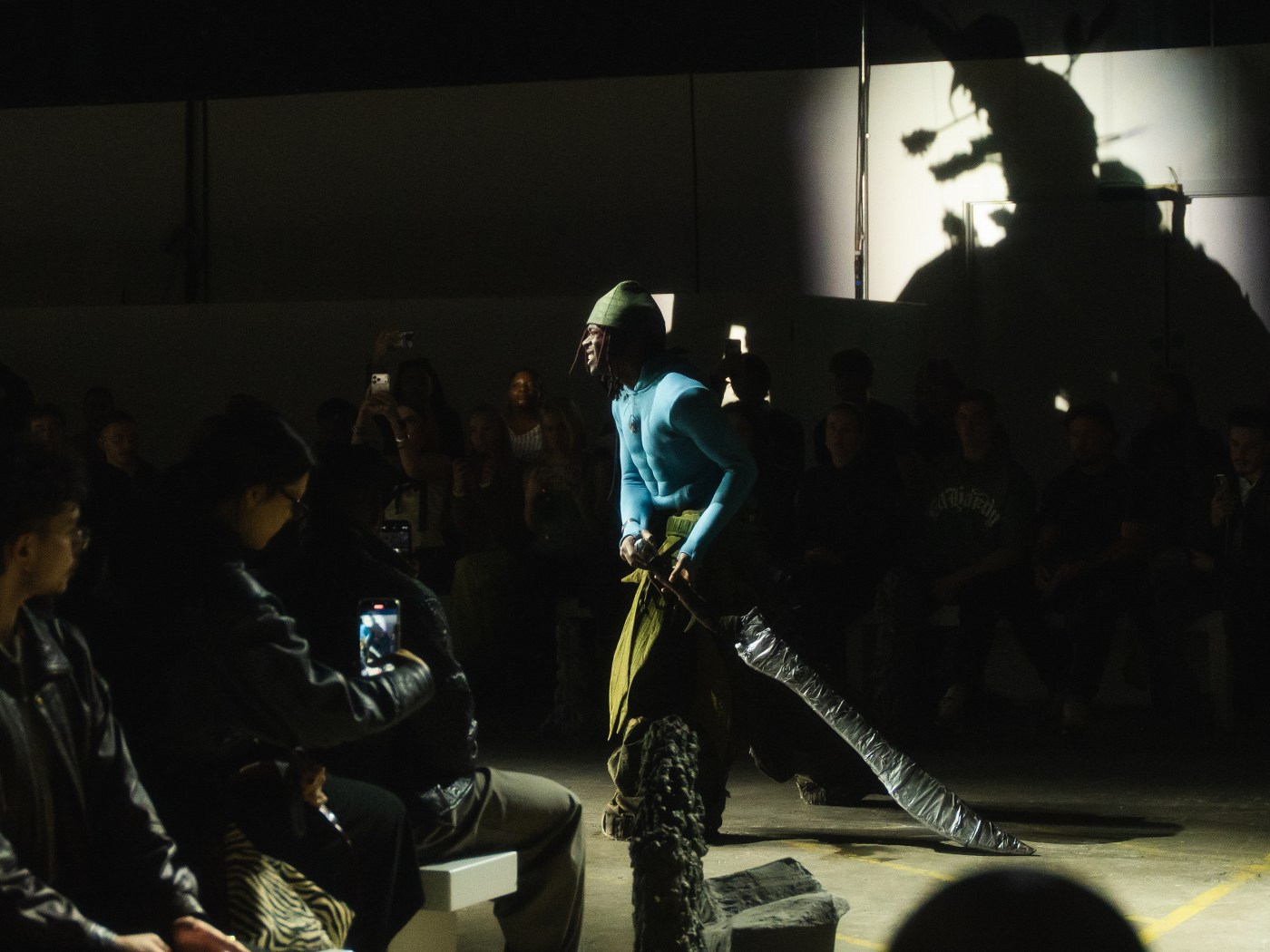 Fashion model on runway with dramatic shadow and audience capturing the moment.