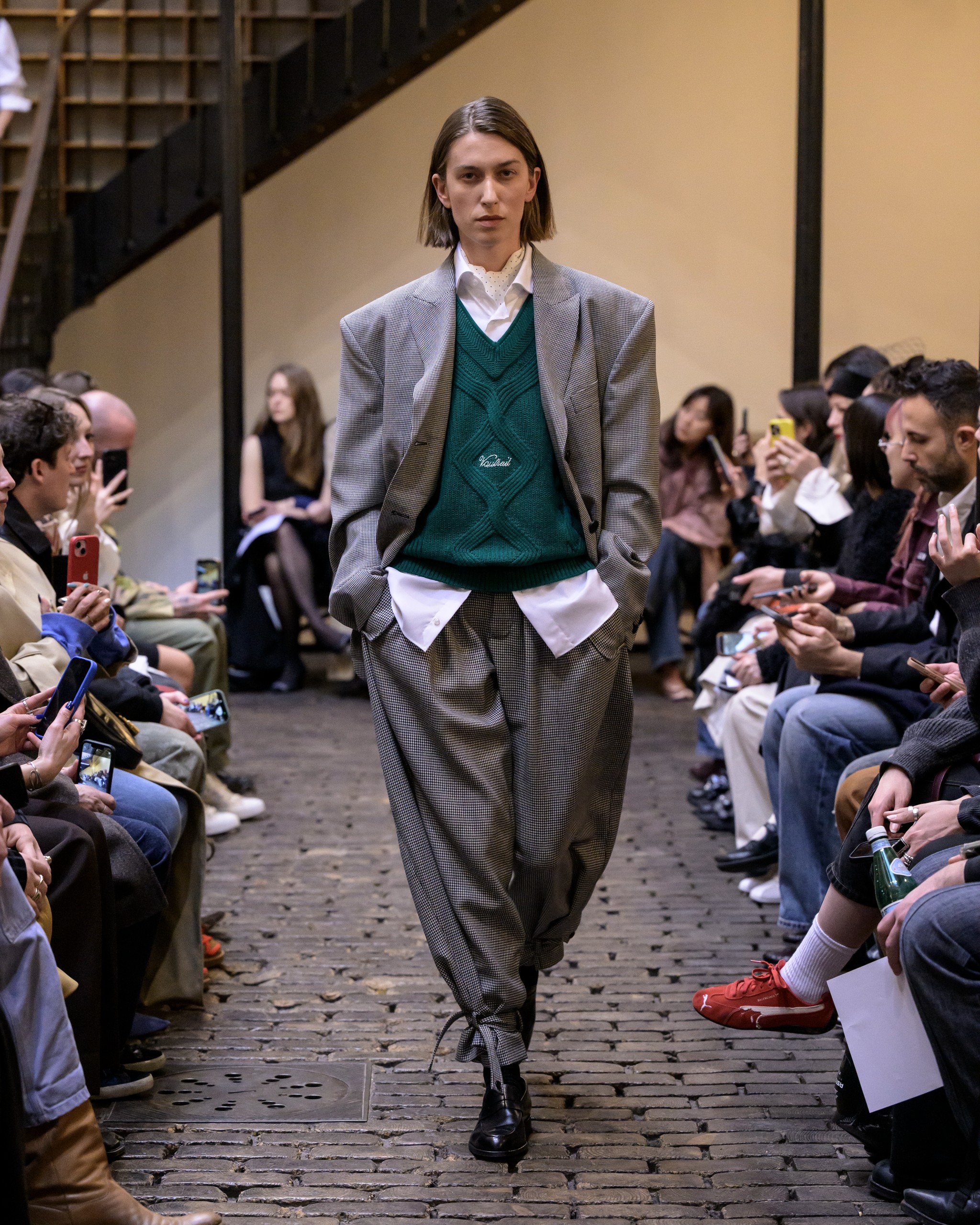 Model in oversized suit walking on runway during fashion show.