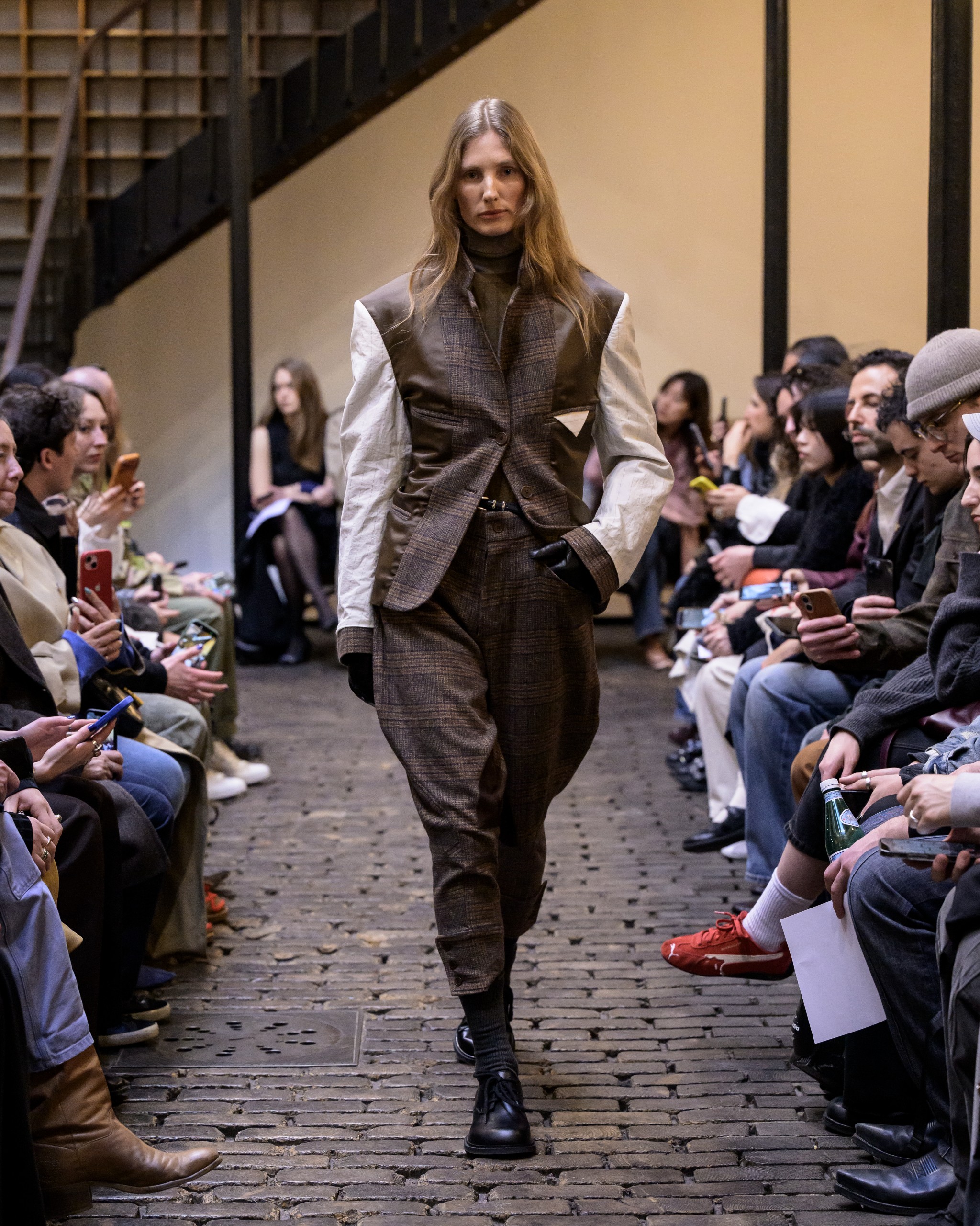 Model in stylish mixed-fabric suit walks runway during a fashion show.
