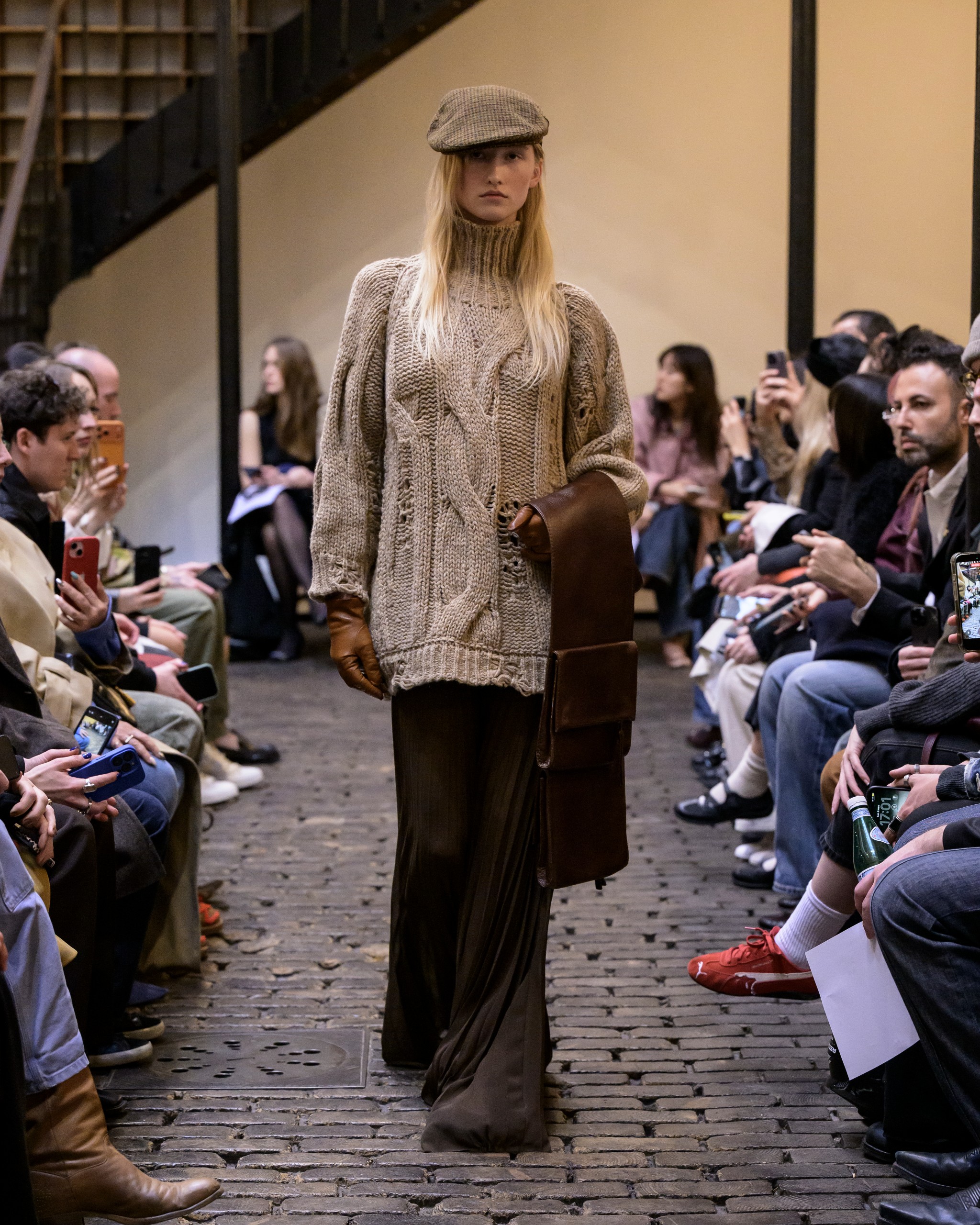 Fashion runway model in cozy knit sweater and cap at a stylish fashion show.