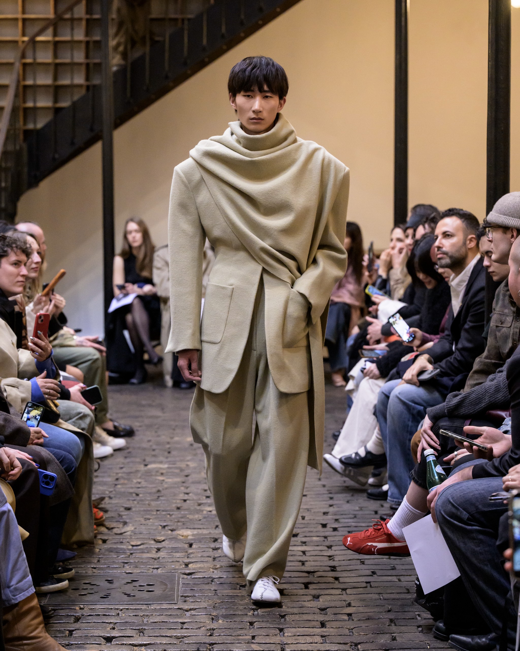 Model in beige fashion outfit walks runway at a stylish fashion show event.
