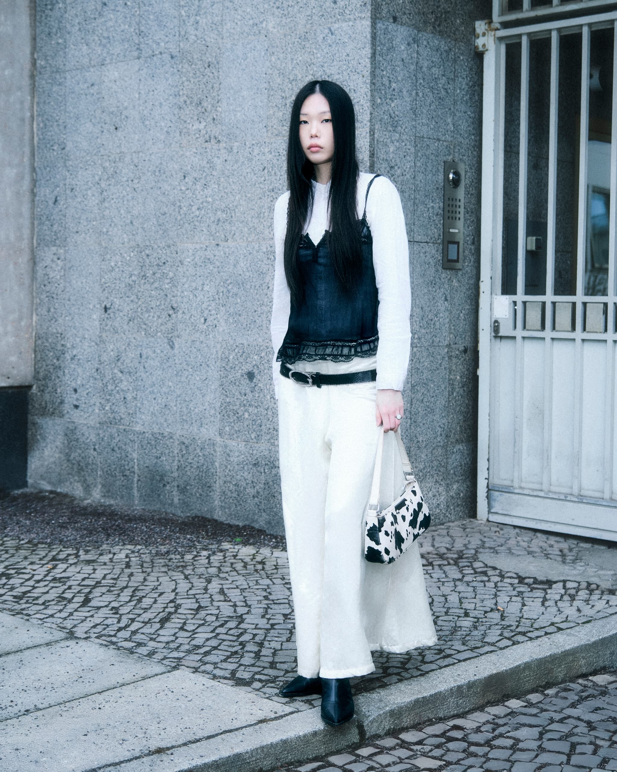 Woman in streetwear with black top, white pants, and cow print bag.