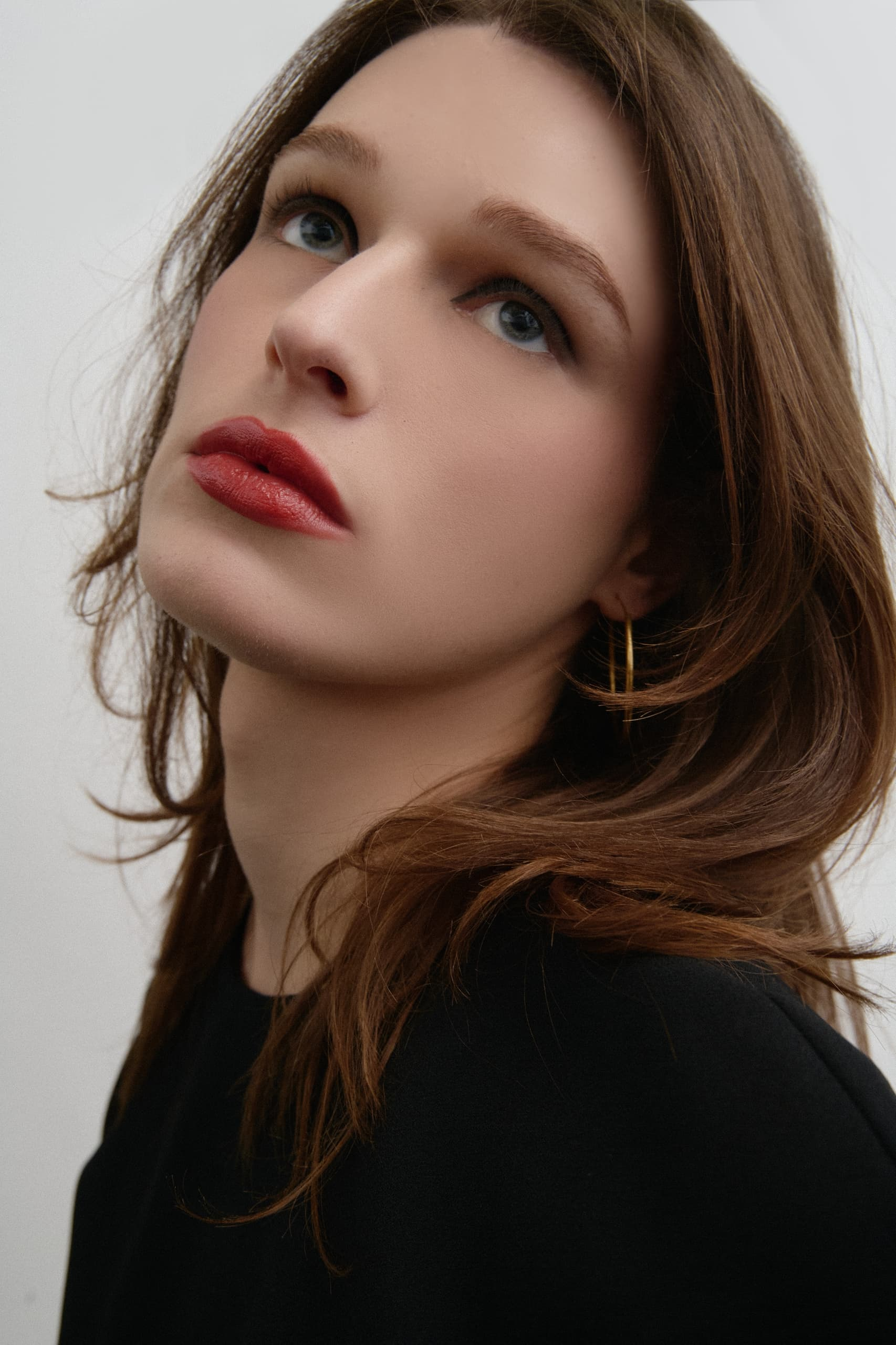 Portrait of a person with long hair and red lips, wearing a black top and gold hoop earring.