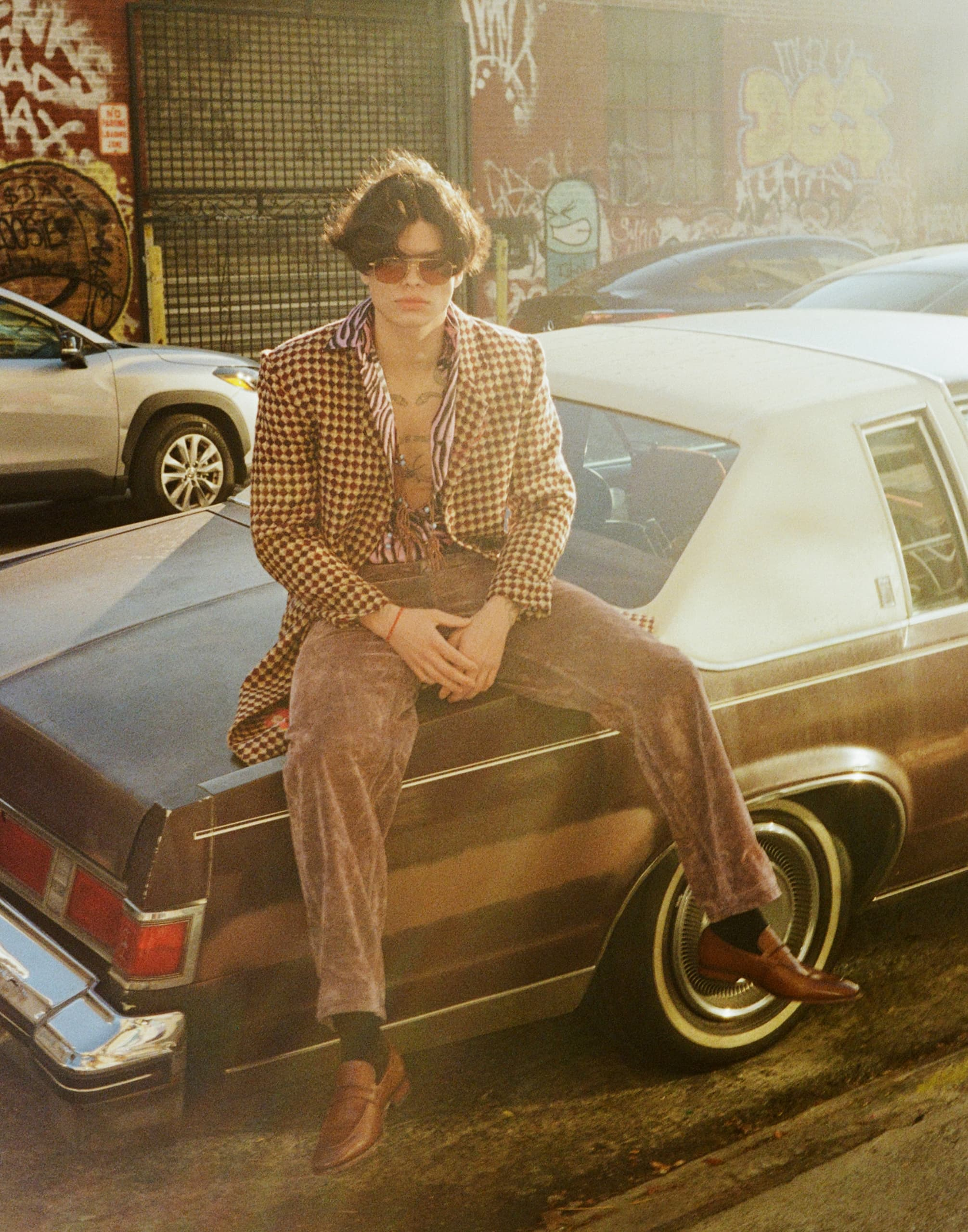 Vintage style person sitting on a classic car in an urban graffiti setting.