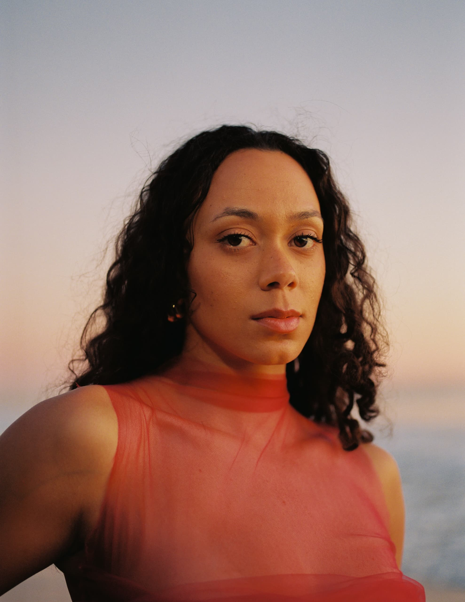 Portrait of woman in red against a serene sunset background.