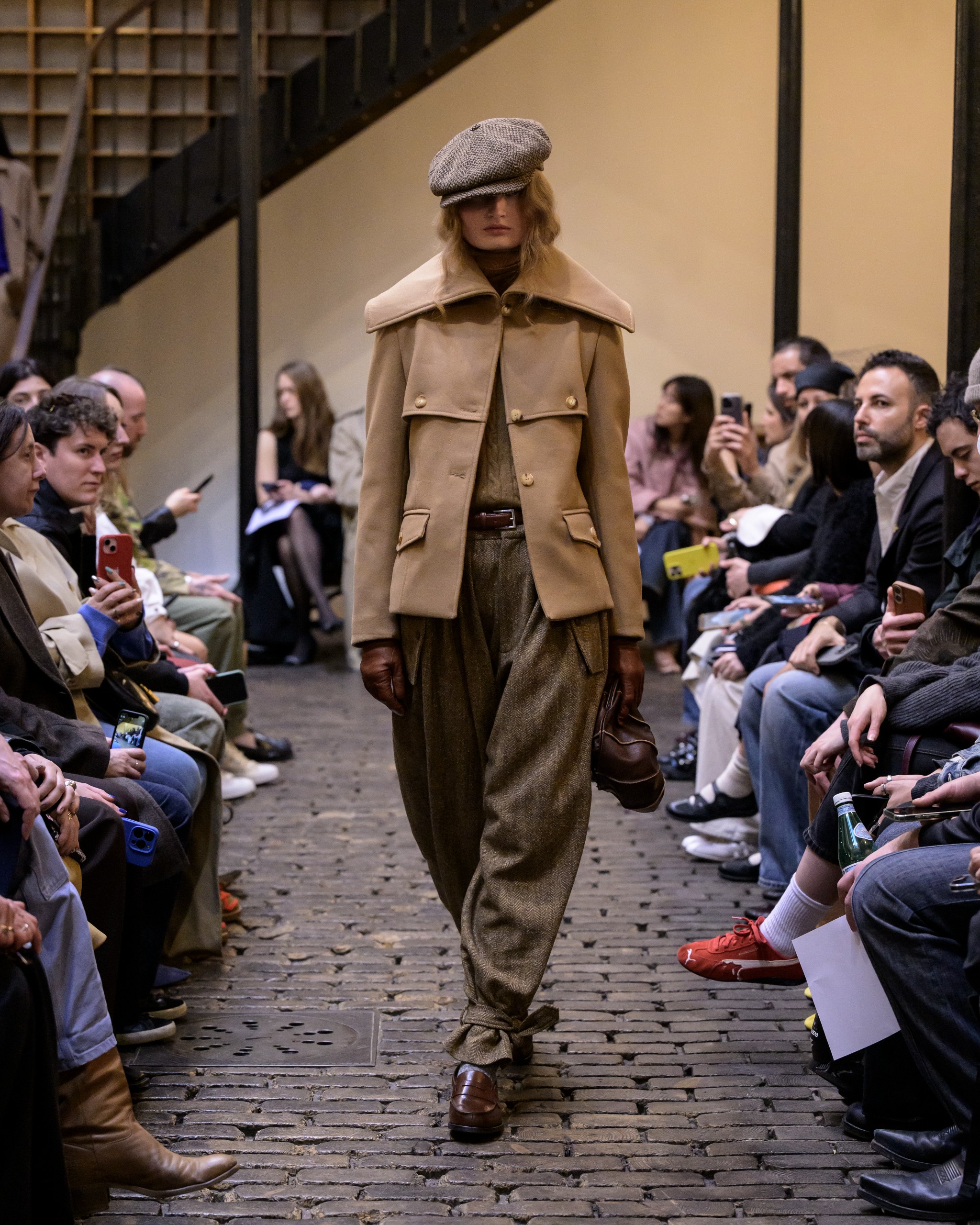 Model in stylish brown outfit on runway at fashion show.
