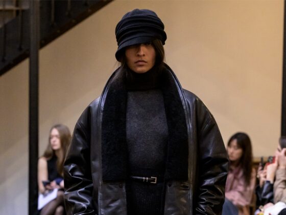 Model showcasing winter fashion at runway event, wearing layered dark attire.