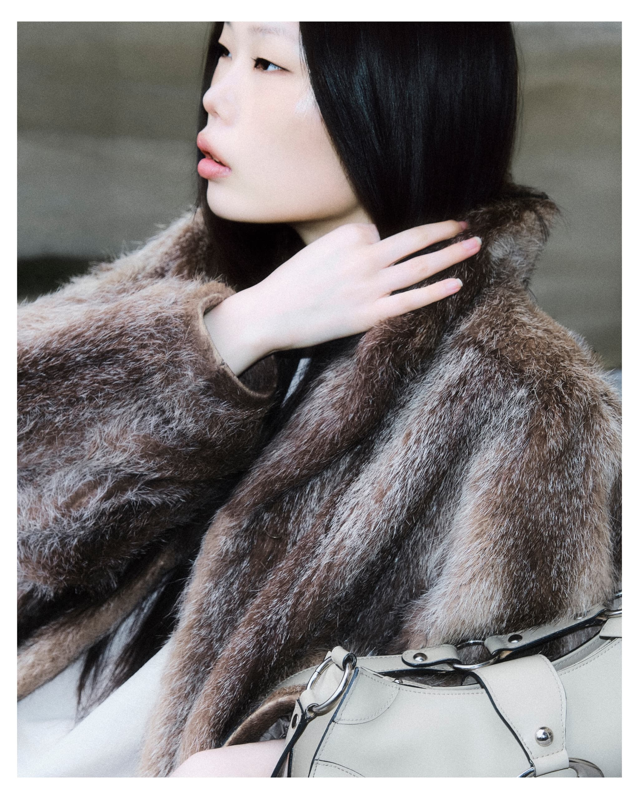 Woman in fur coat with handbag, looking pensive, hand touching hair.