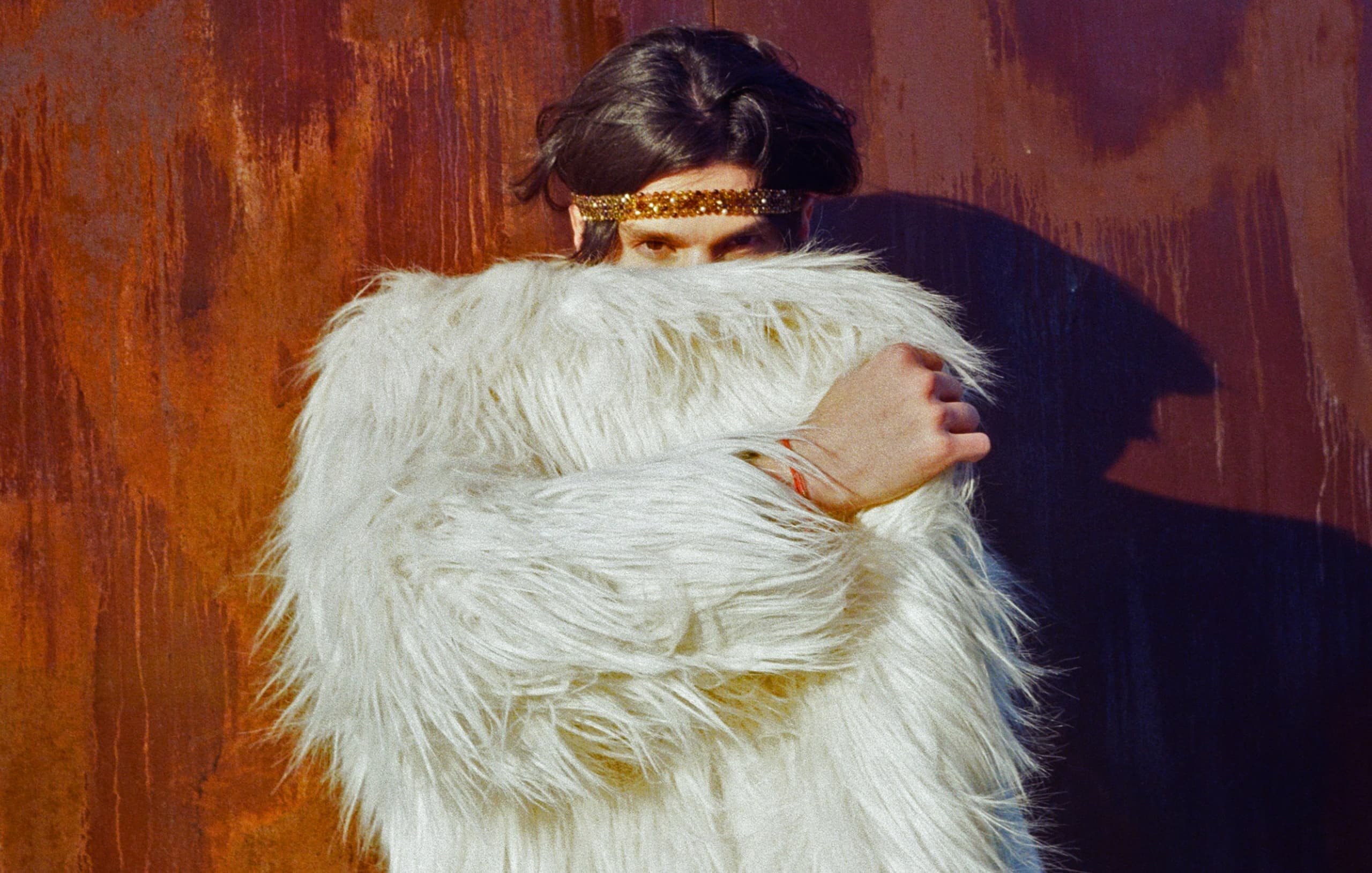 Person in fluffy white coat with gold headband, mysterious look, rustic background.