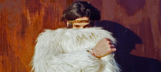 Person in white furry coat with gold headband against a textured wall. Fashion statement.