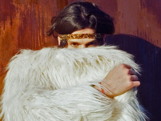 Person in white furry coat with gold headband against a textured wall. Fashion statement.