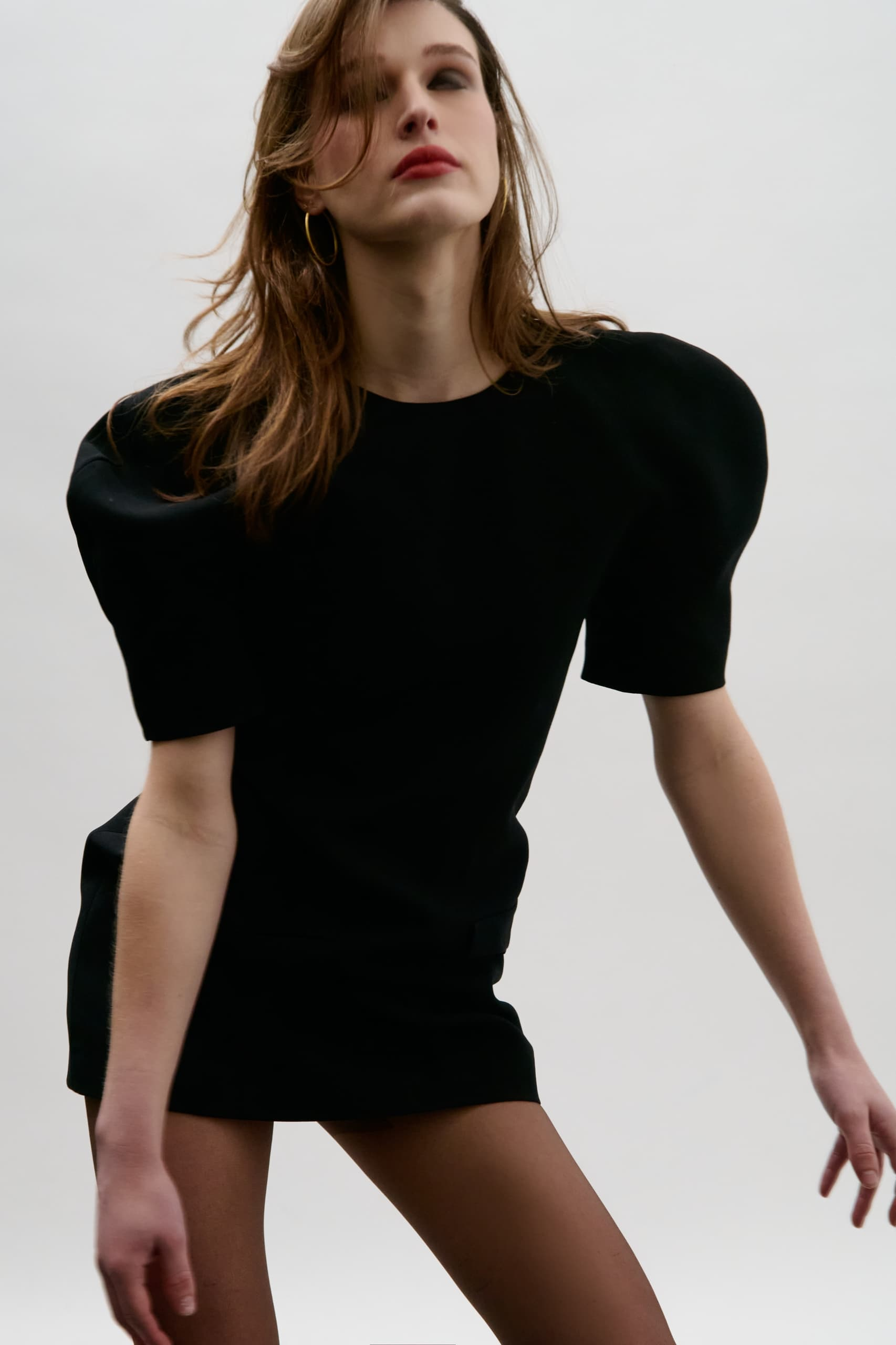 Fashion model in a striking black dress posing with a confident expression.