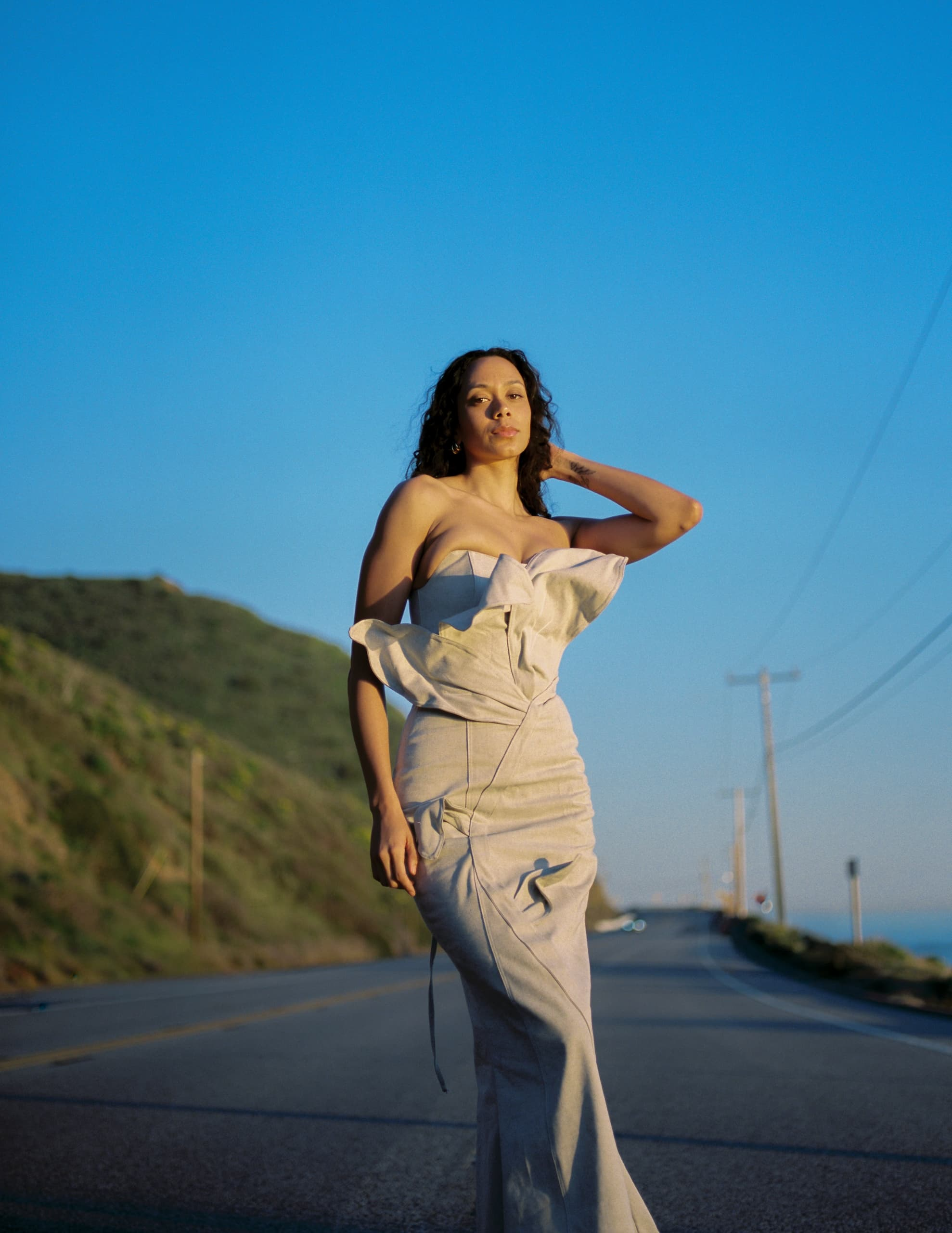 Woman in elegant dress walking on scenic road at sunset.