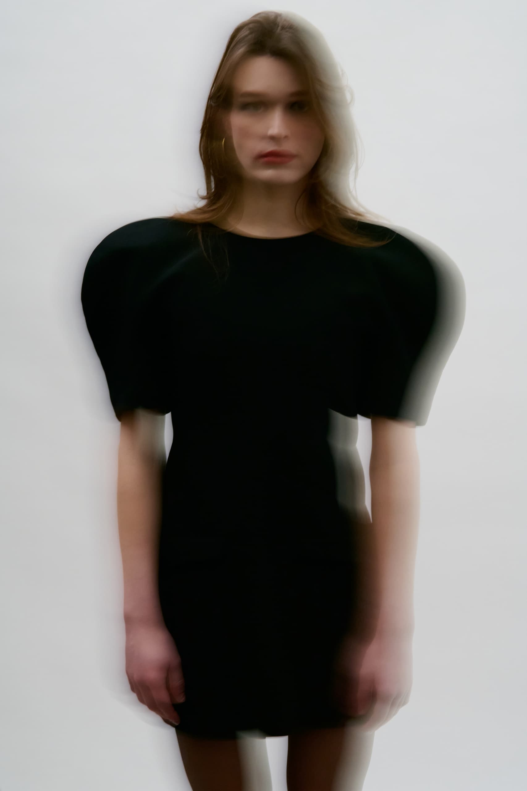 Blurry woman in black dress with puff sleeves on a plain background.