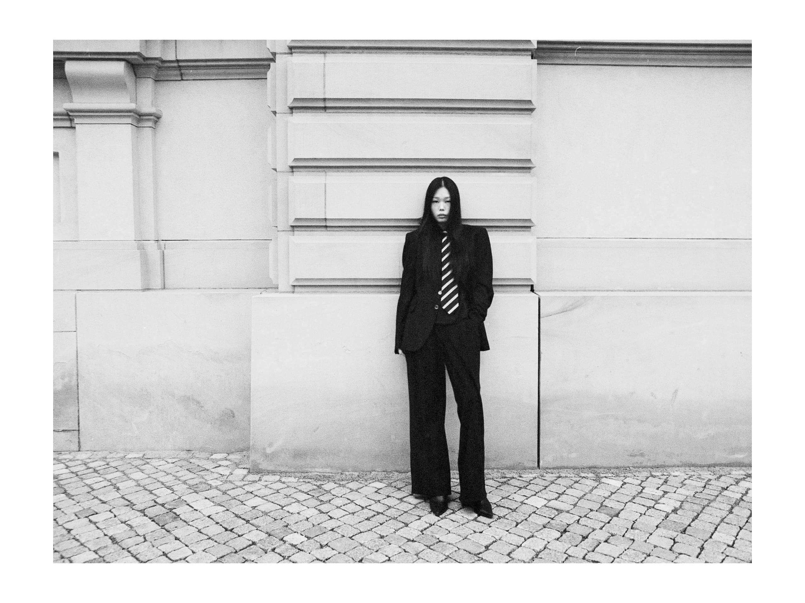 Person in a suit with a striped tie standing against a decorative stone wall.