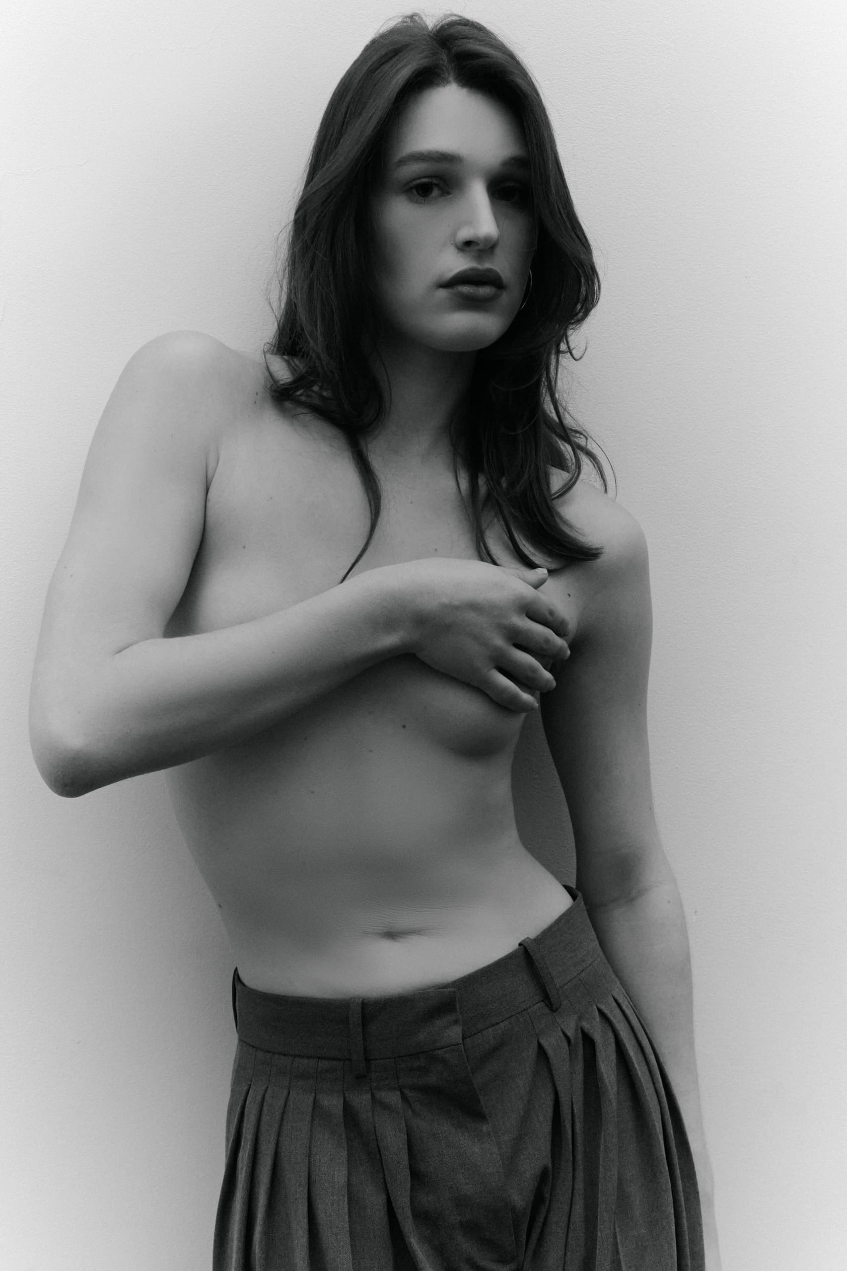 Black and white portrait of a person in pleated trousers, hand on chest.
