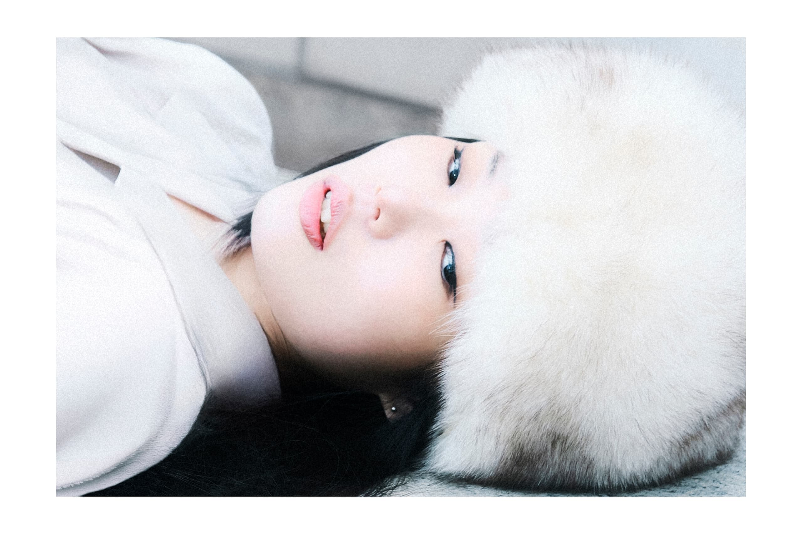 Woman in a white fur hat lying down, gazing upward with a serene expression.