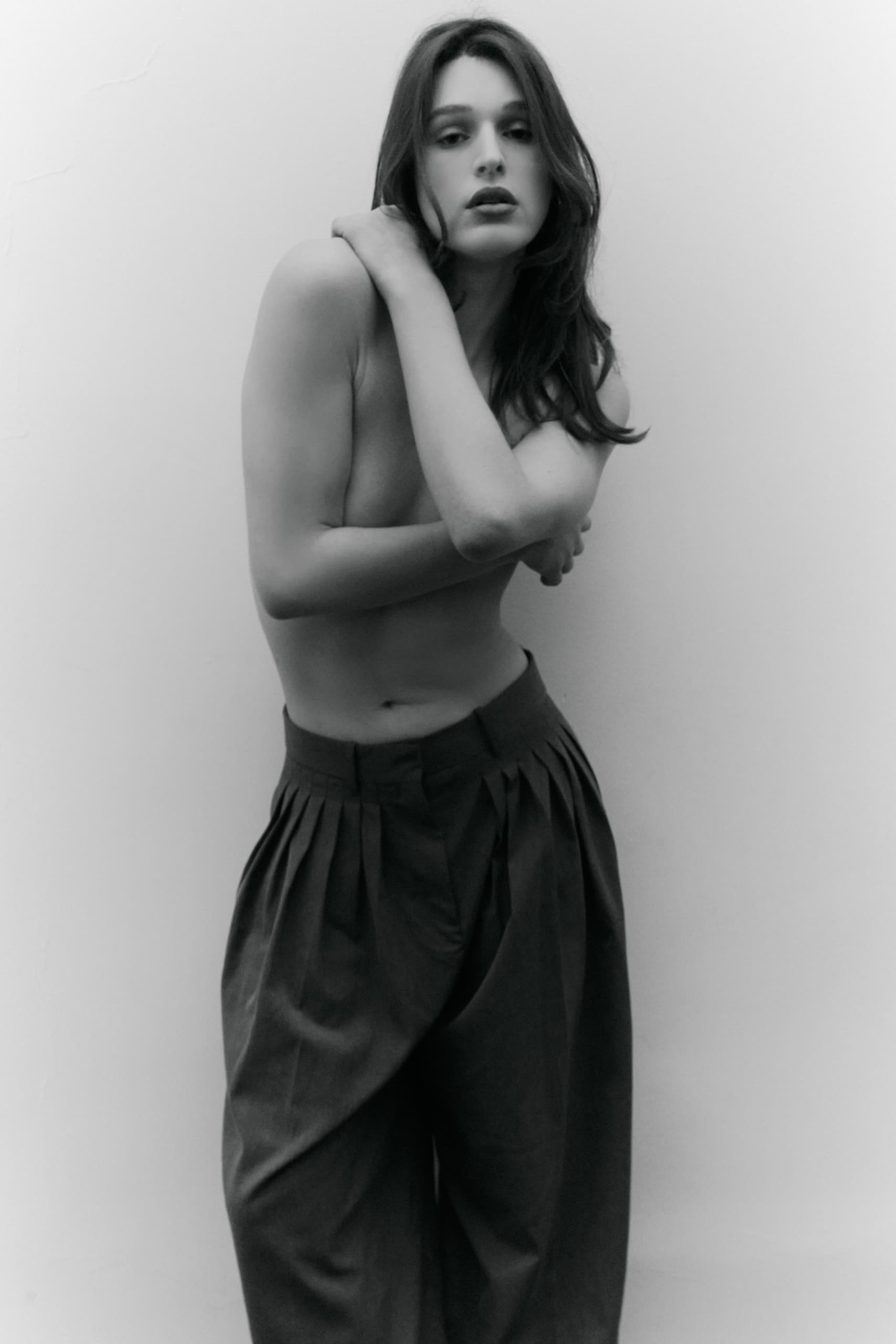 Black and white photo of a person posing with arms crossed, wearing wide-leg pants.