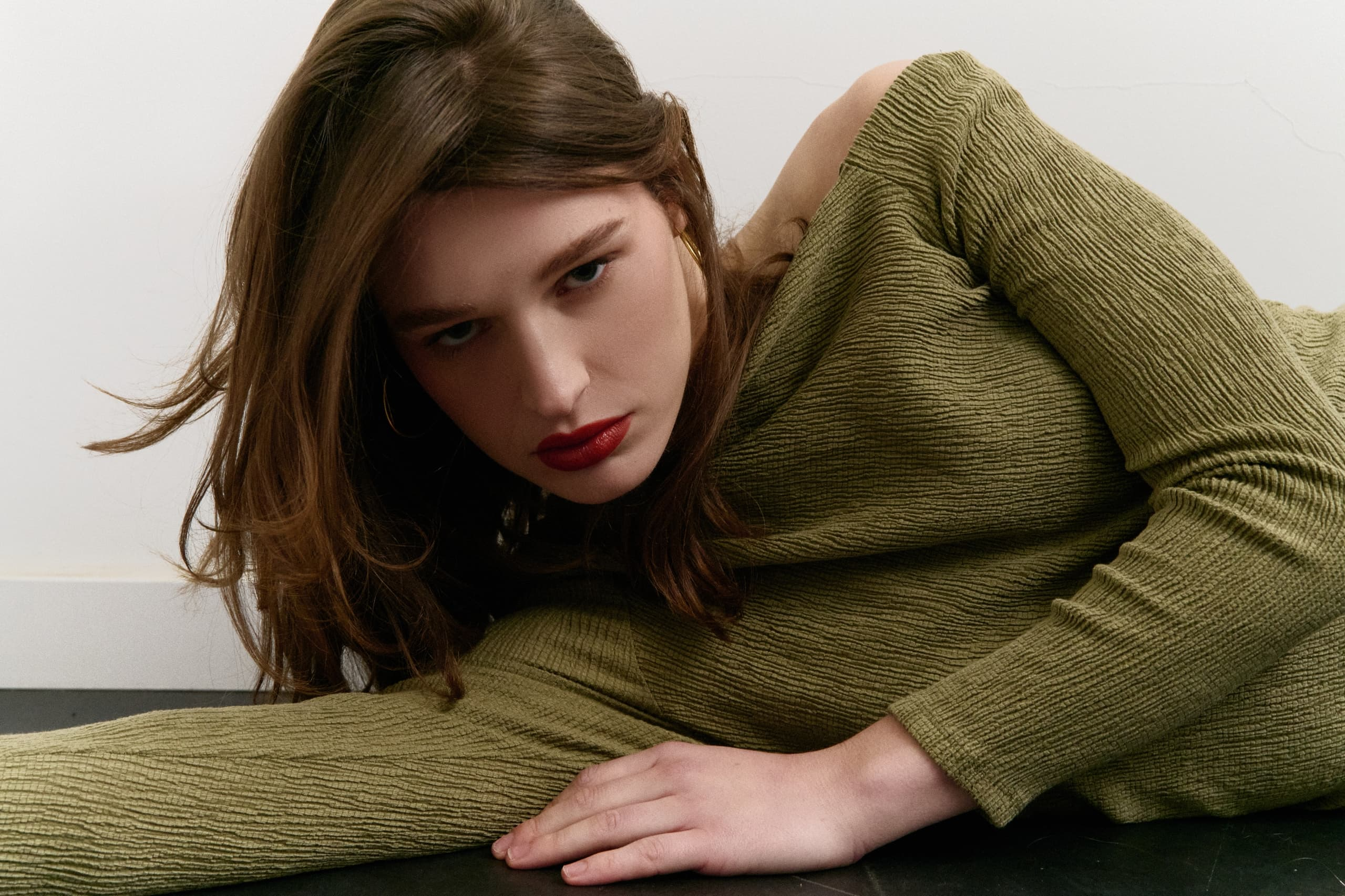 Person in green outfit lying on the floor with a focused expression.