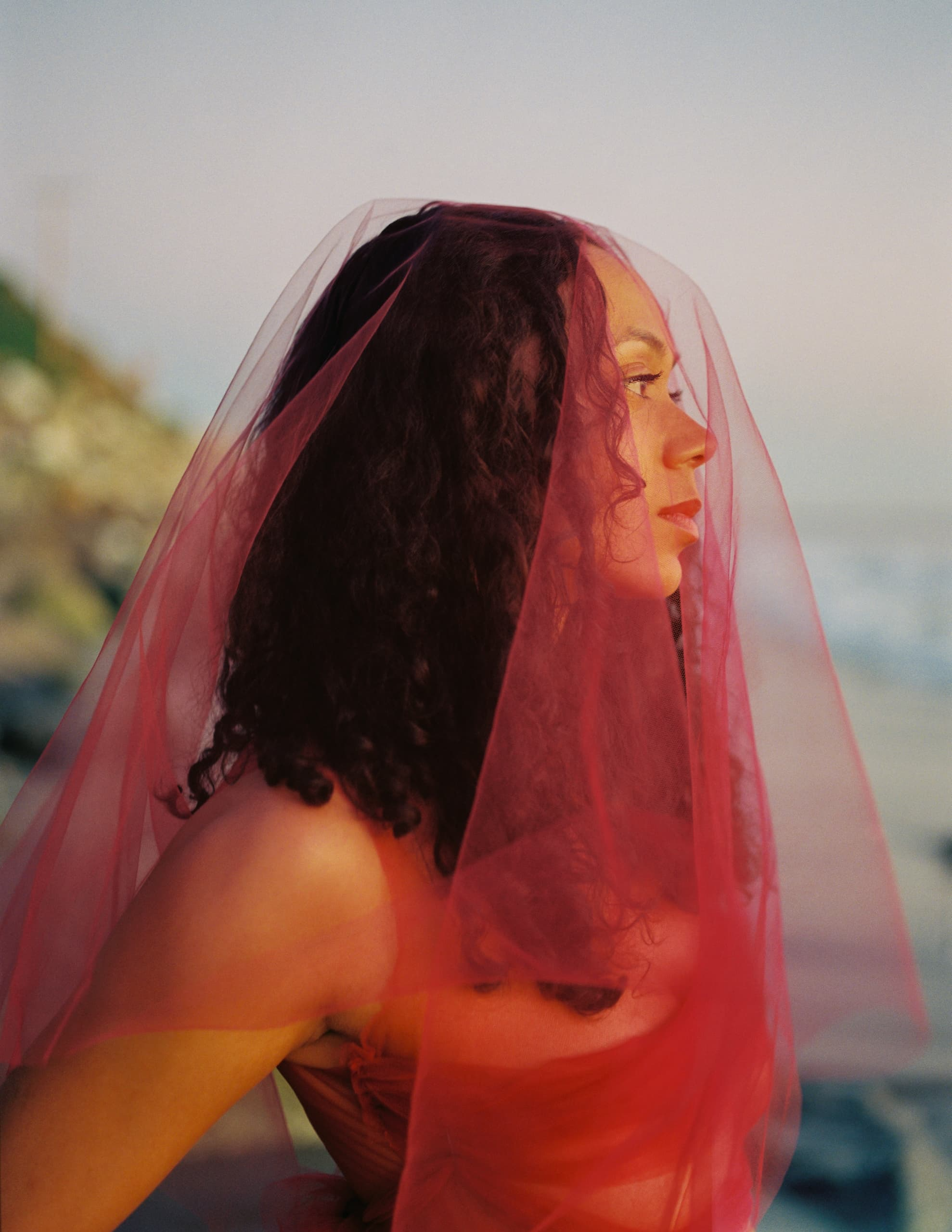 Woman in red veil gazing at sunset by the sea.