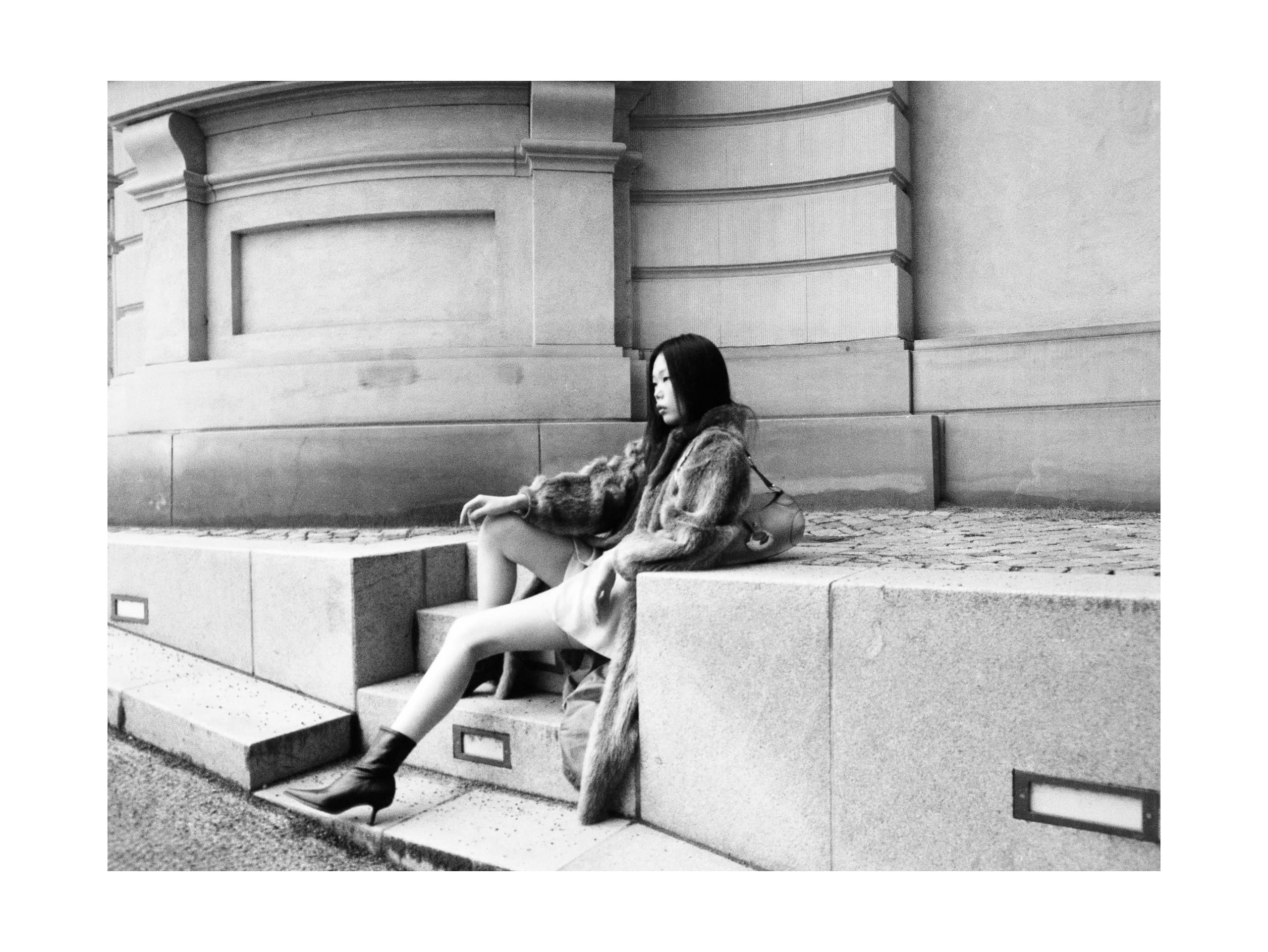 Woman in a fur coat sitting on urban steps, black-and-white photo.