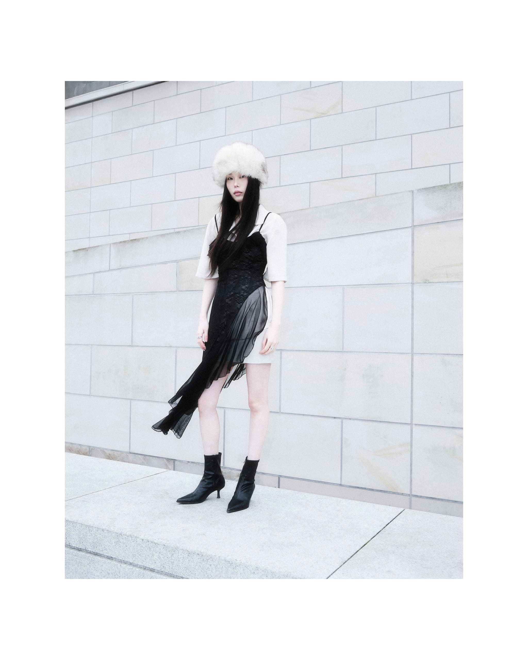 Fashionable woman in urban setting, styled in chic black dress and fur hat.