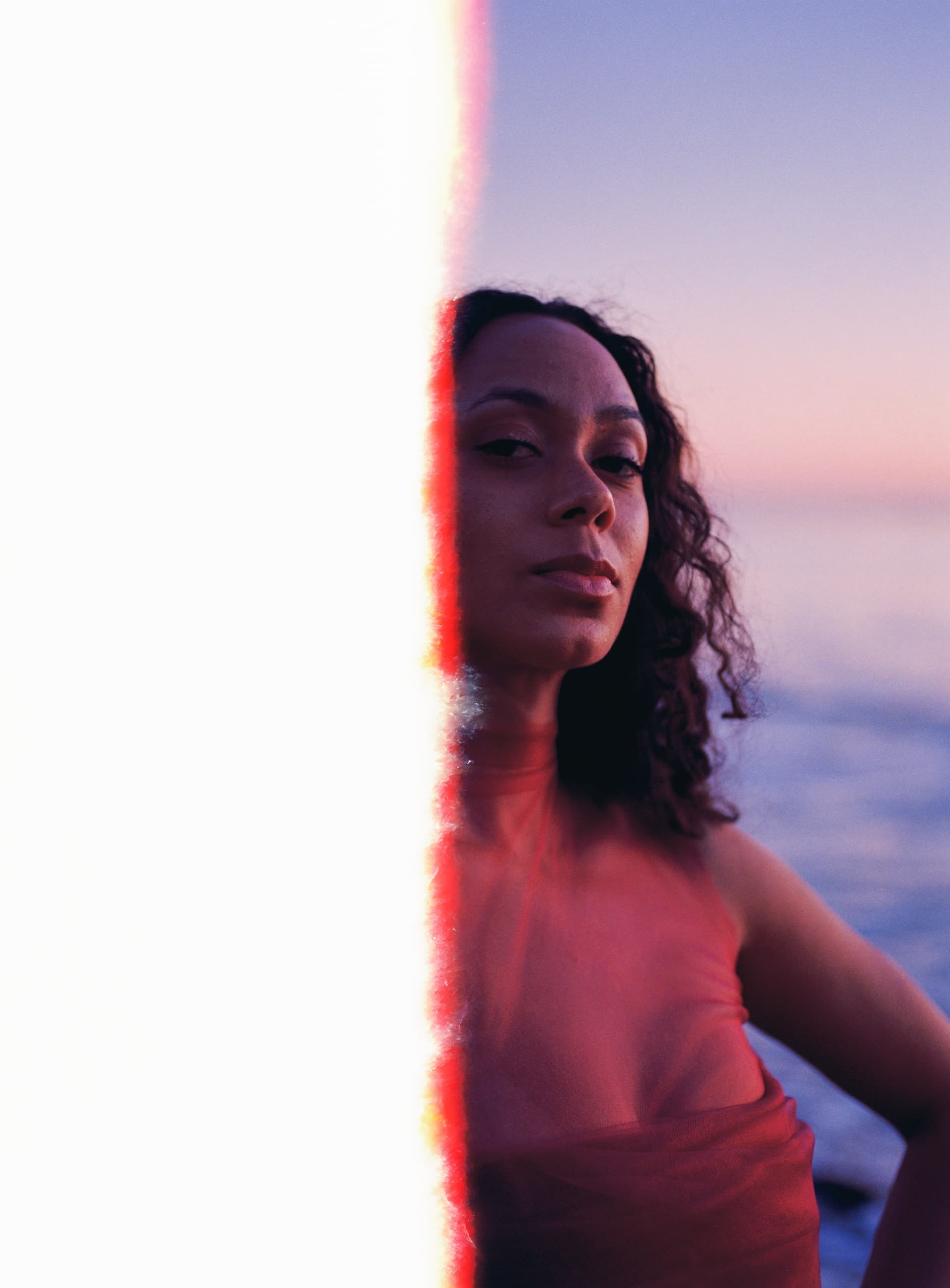 Portrait with vintage film light leak, woman in red against ocean sunset backdrop.