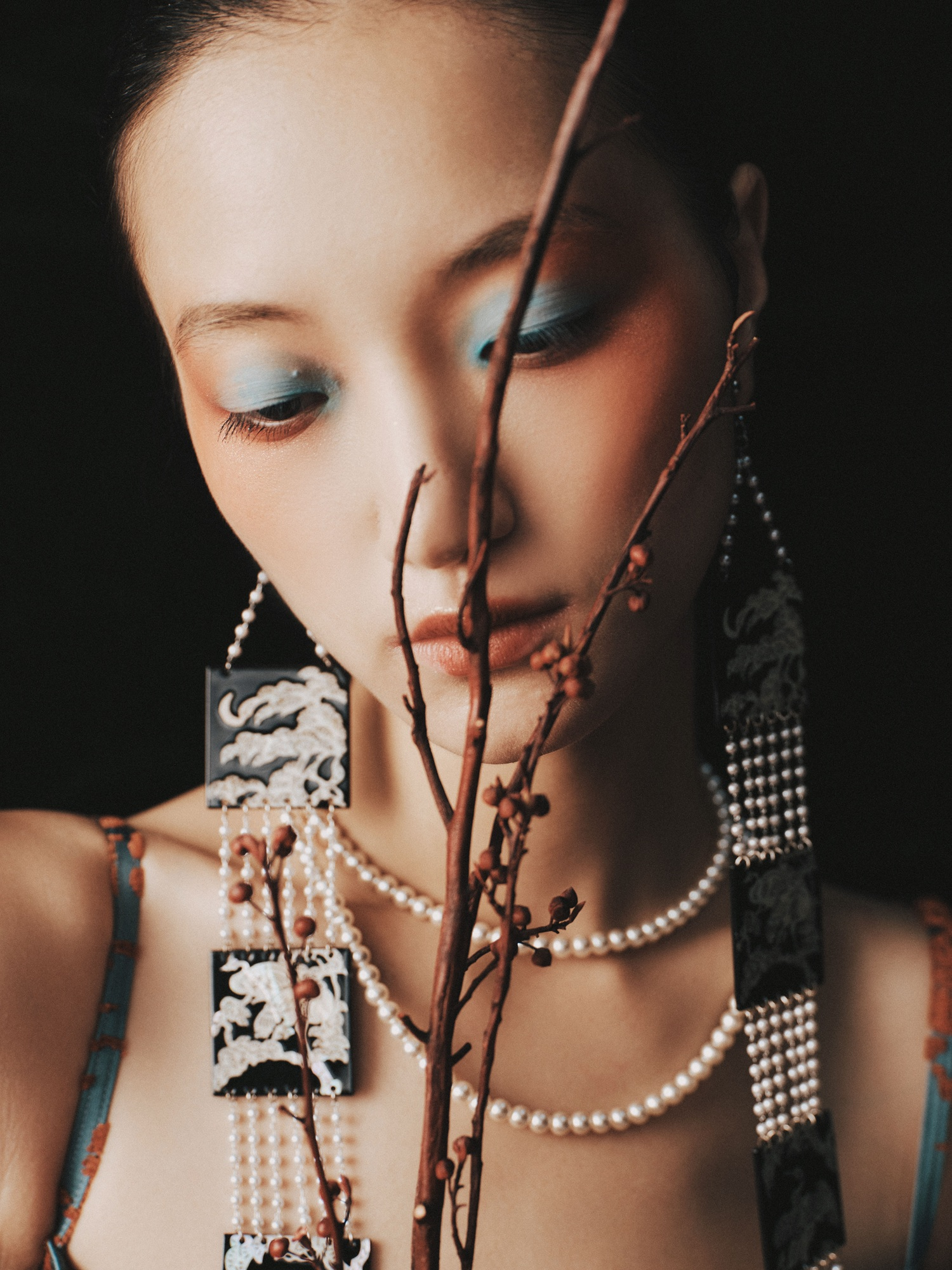 Elegant woman with creative makeup and jewelry, adorned with branch accents.