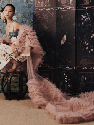 Elegant woman in floral attire with luxurious pink robe in ornate room.