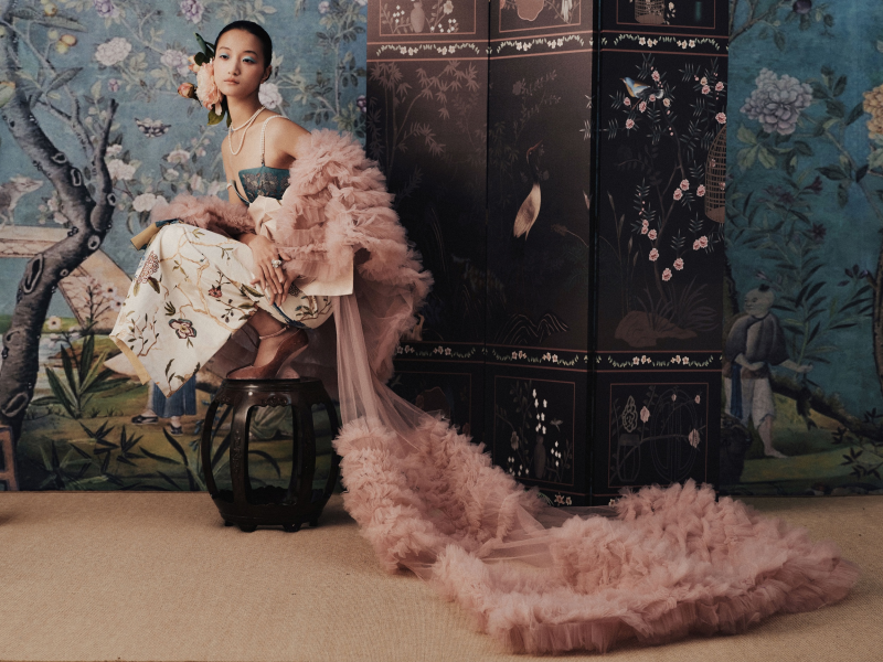 Elegant woman in floral attire with luxurious pink robe in ornate room.