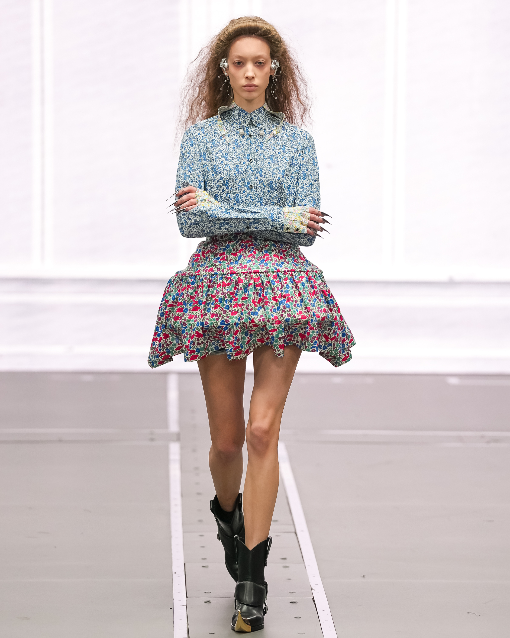 Model in floral outfit struts runway in chic boots, showcasing latest fashion trends.