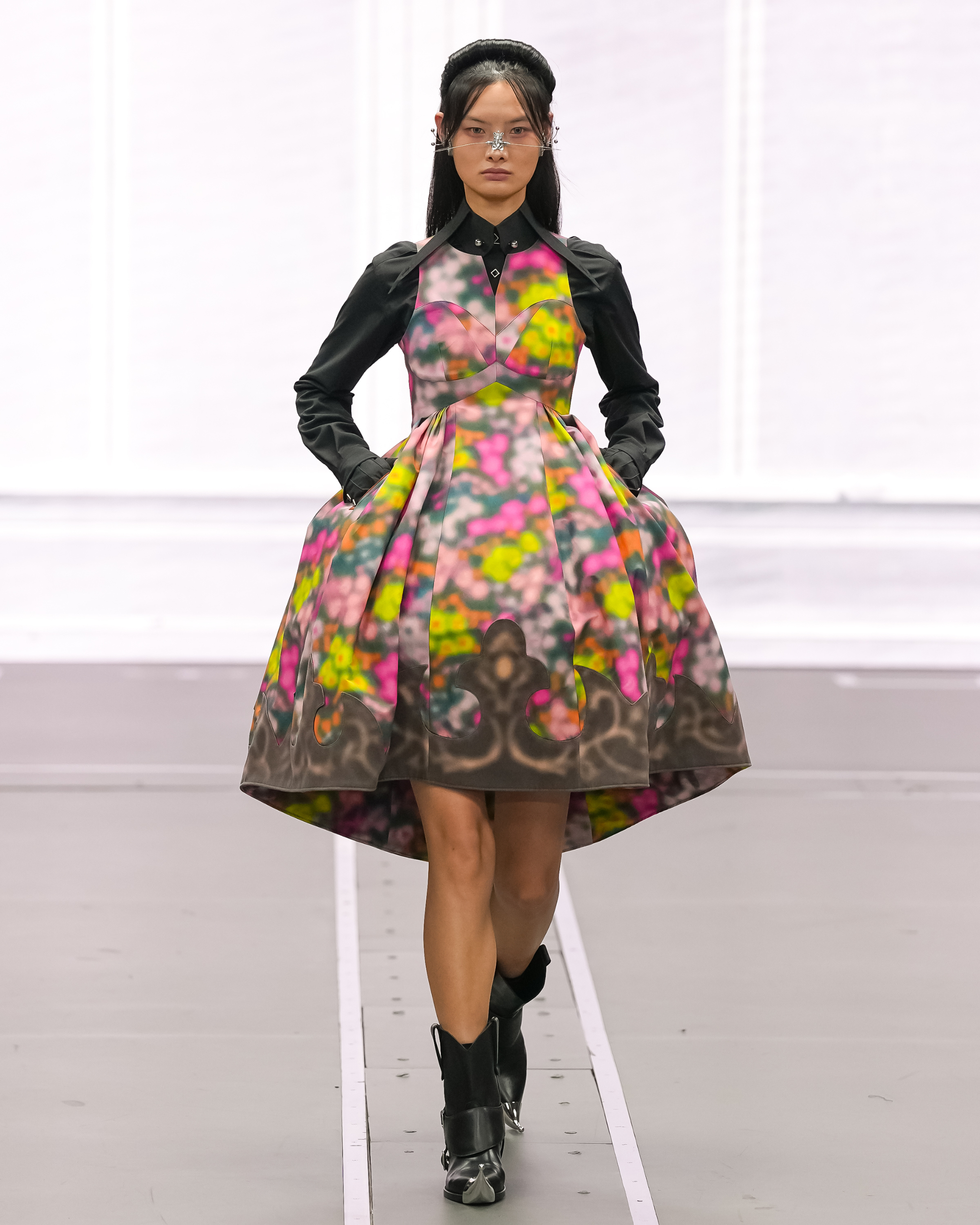 Model showcases colorful floral dress on runway with edgy style.