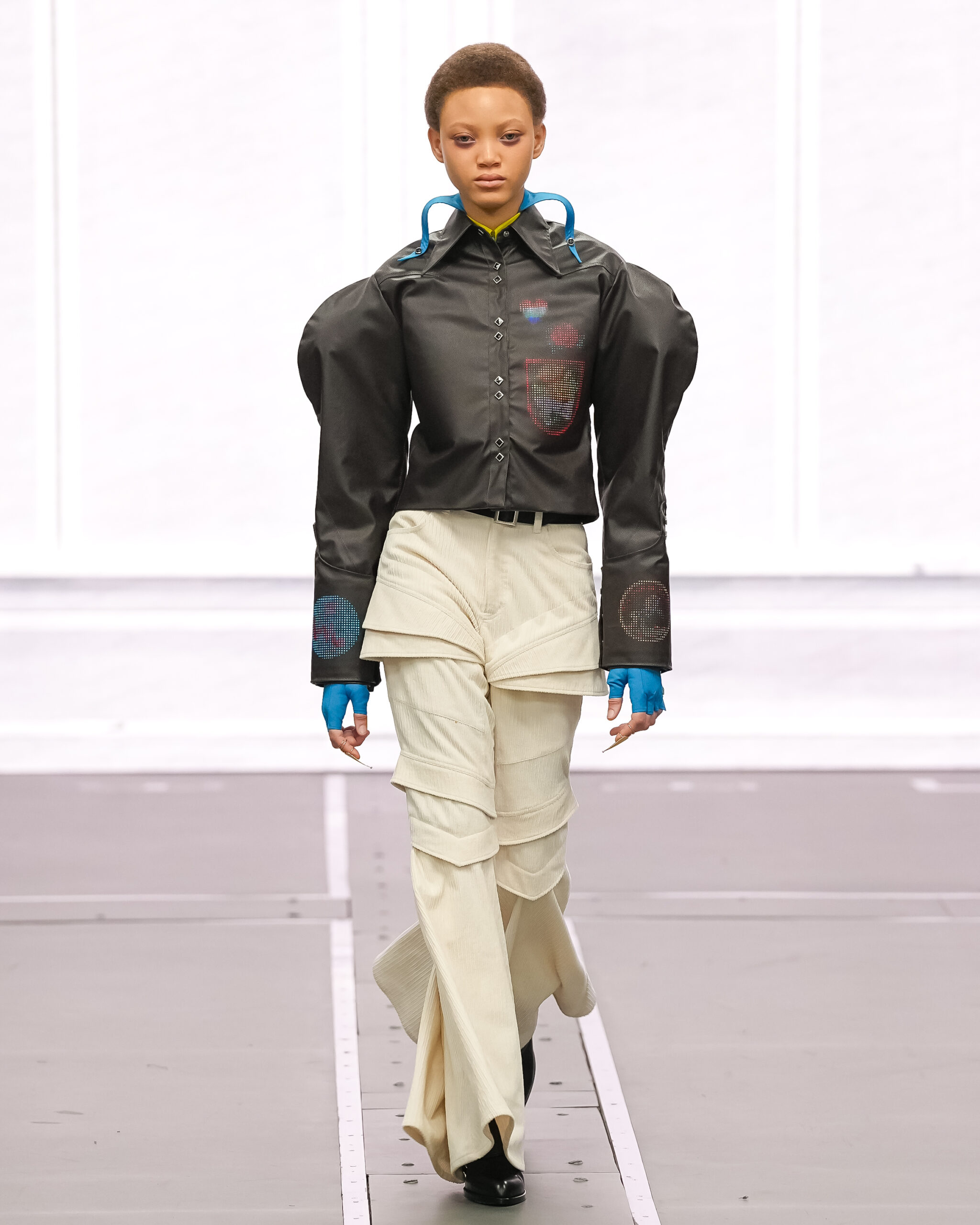 Fashion model walking runway in avant-garde outfit with layered pants.