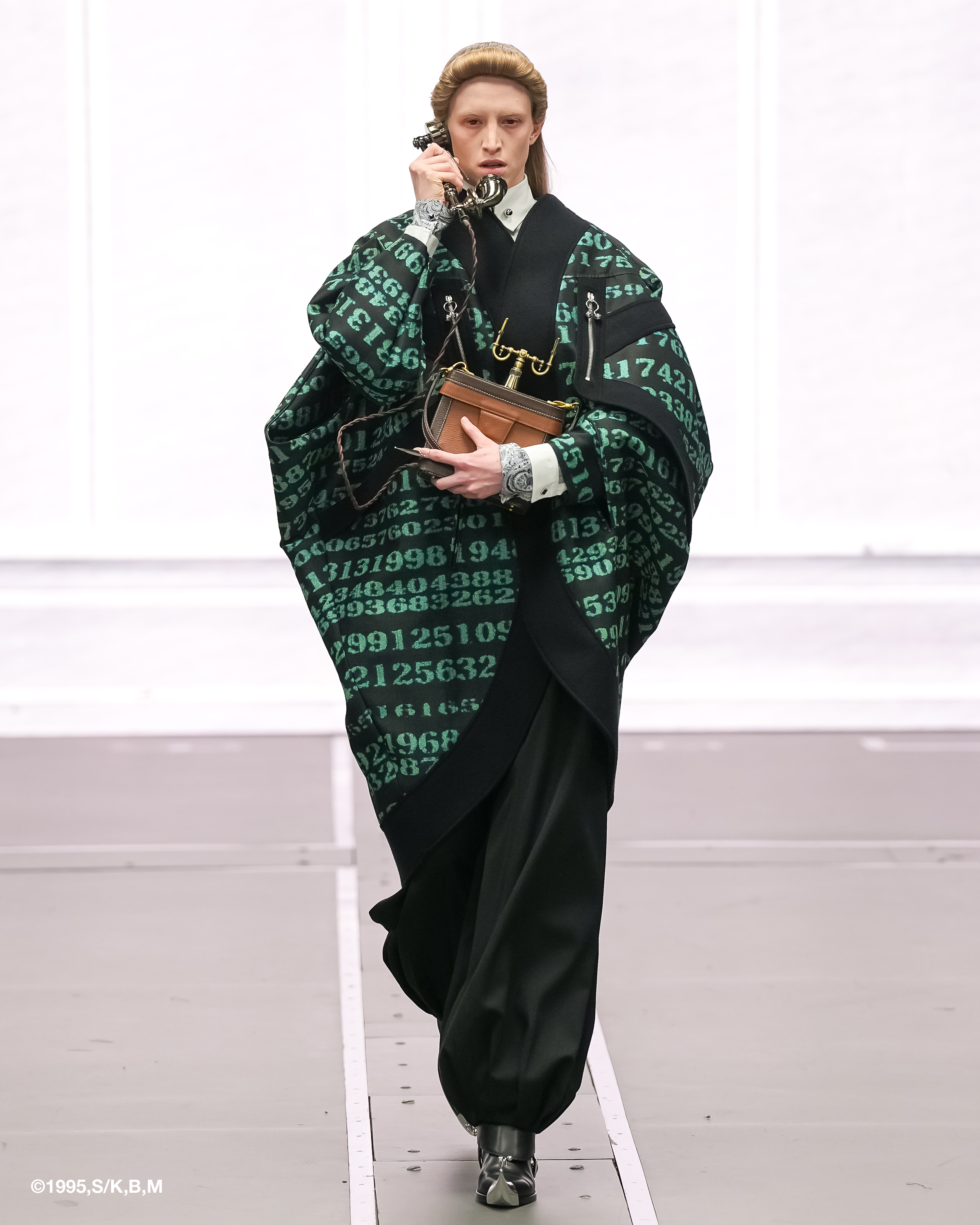 Model in digital print kimono holding a vintage phone on runway.