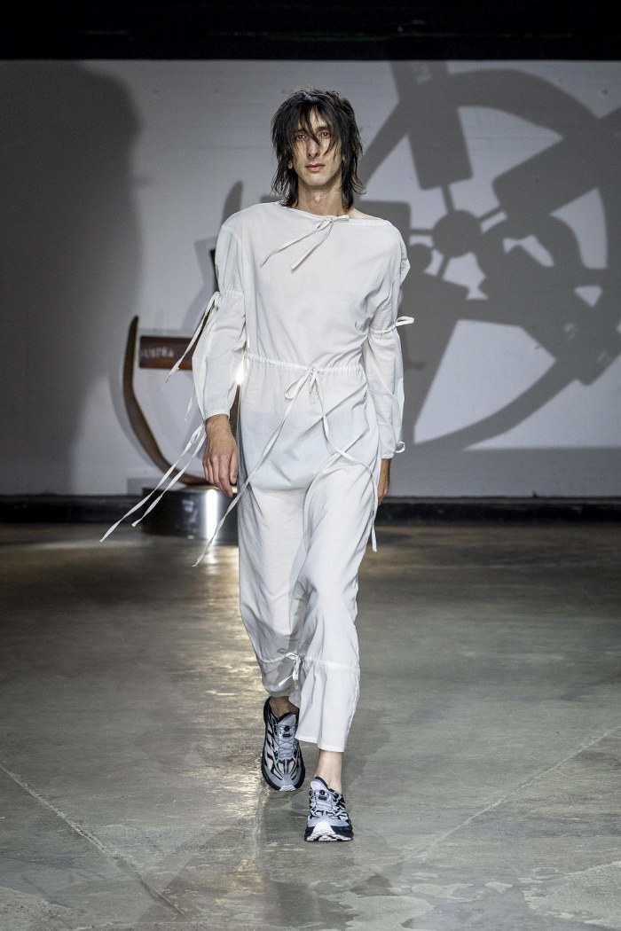 Model in white outfit walking runway at a fashion show.