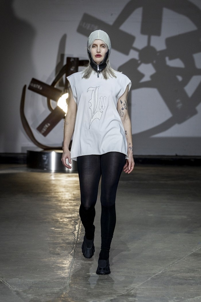 Model in edgy fashion walking runway in minimalist industrial setting.