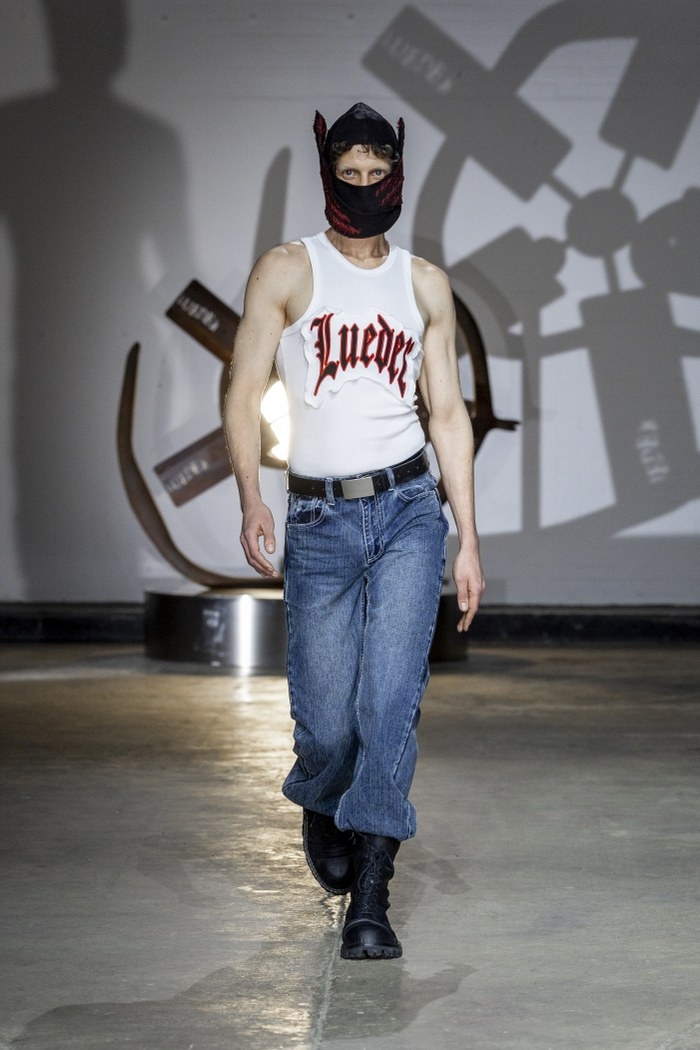 Model in mask and casual outfit on runway with abstract background.