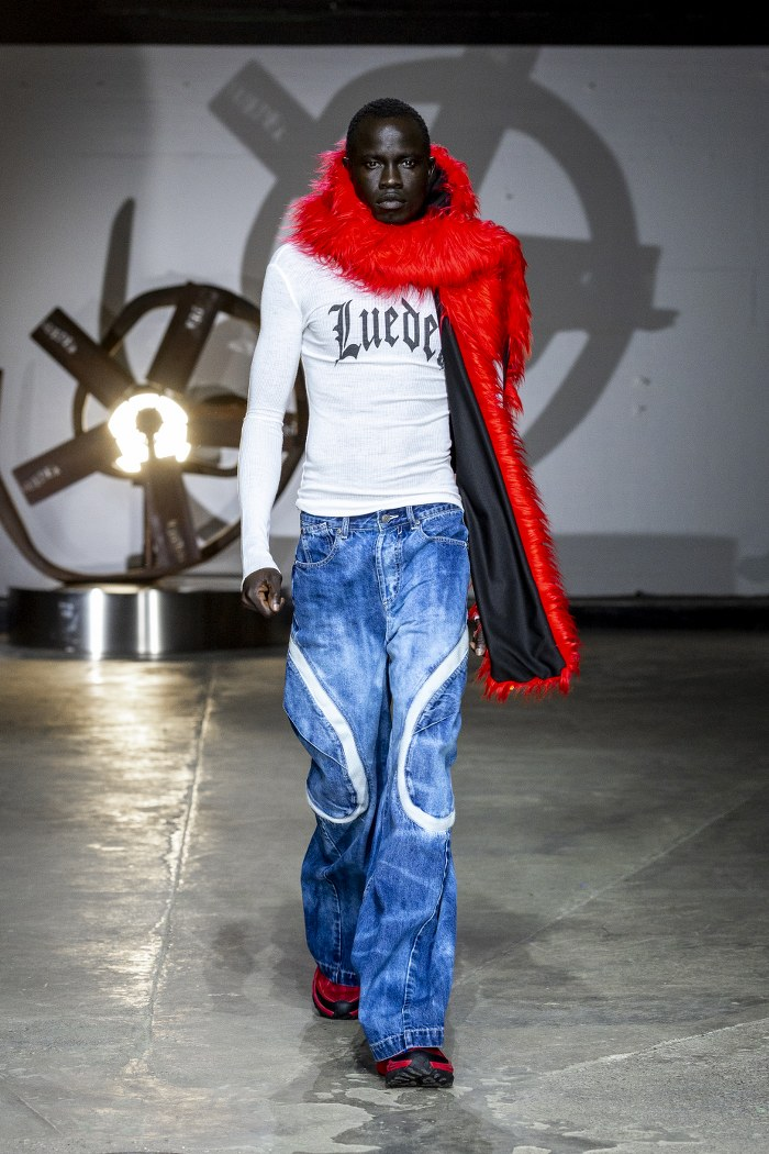 Model in bold fashion with red fur scarf and jeans on runway.