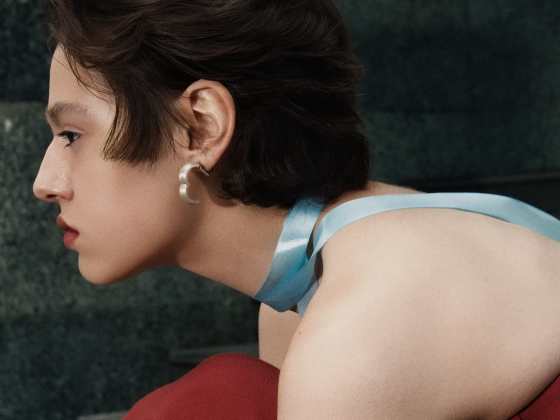 Person with a blue ribbon choker and a red top, accessorizing with hoop earrings.