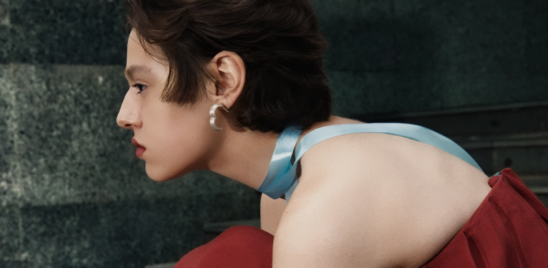 Person with a blue ribbon choker and a red top, accessorizing with hoop earrings.