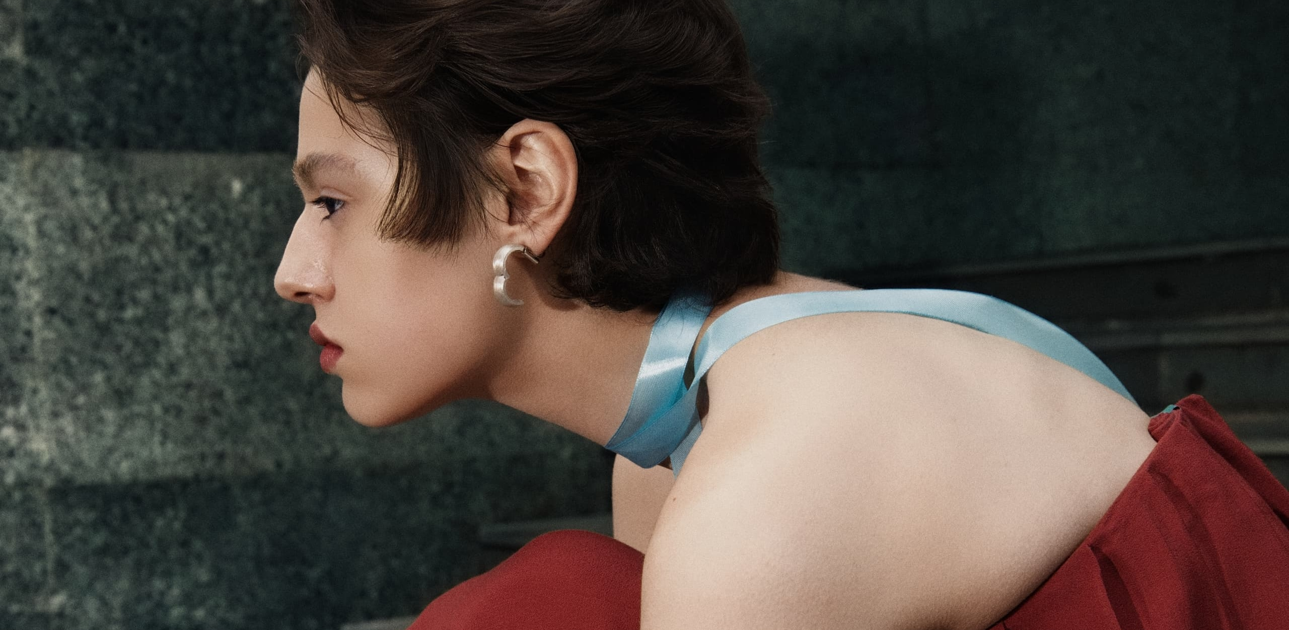 Person with a blue ribbon choker and a red top, accessorizing with hoop earrings.