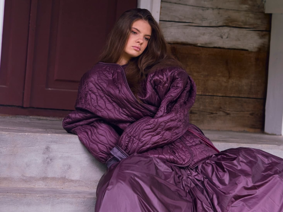 Woman in a purple quilted outfit sitting on steps by a rustic wooden door.