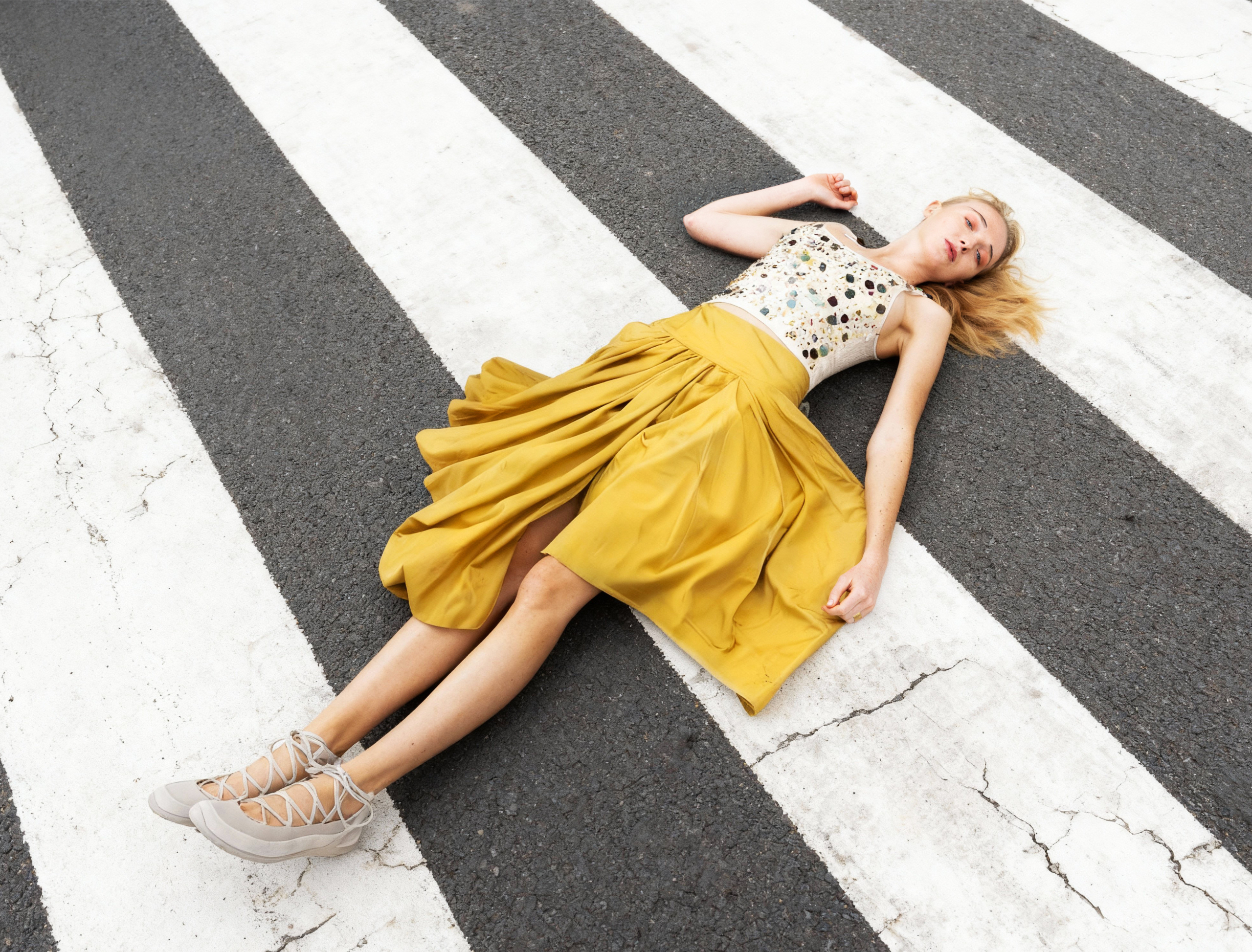 Woman in yellow skirt lying on zebra crossing for a fashion shoot.