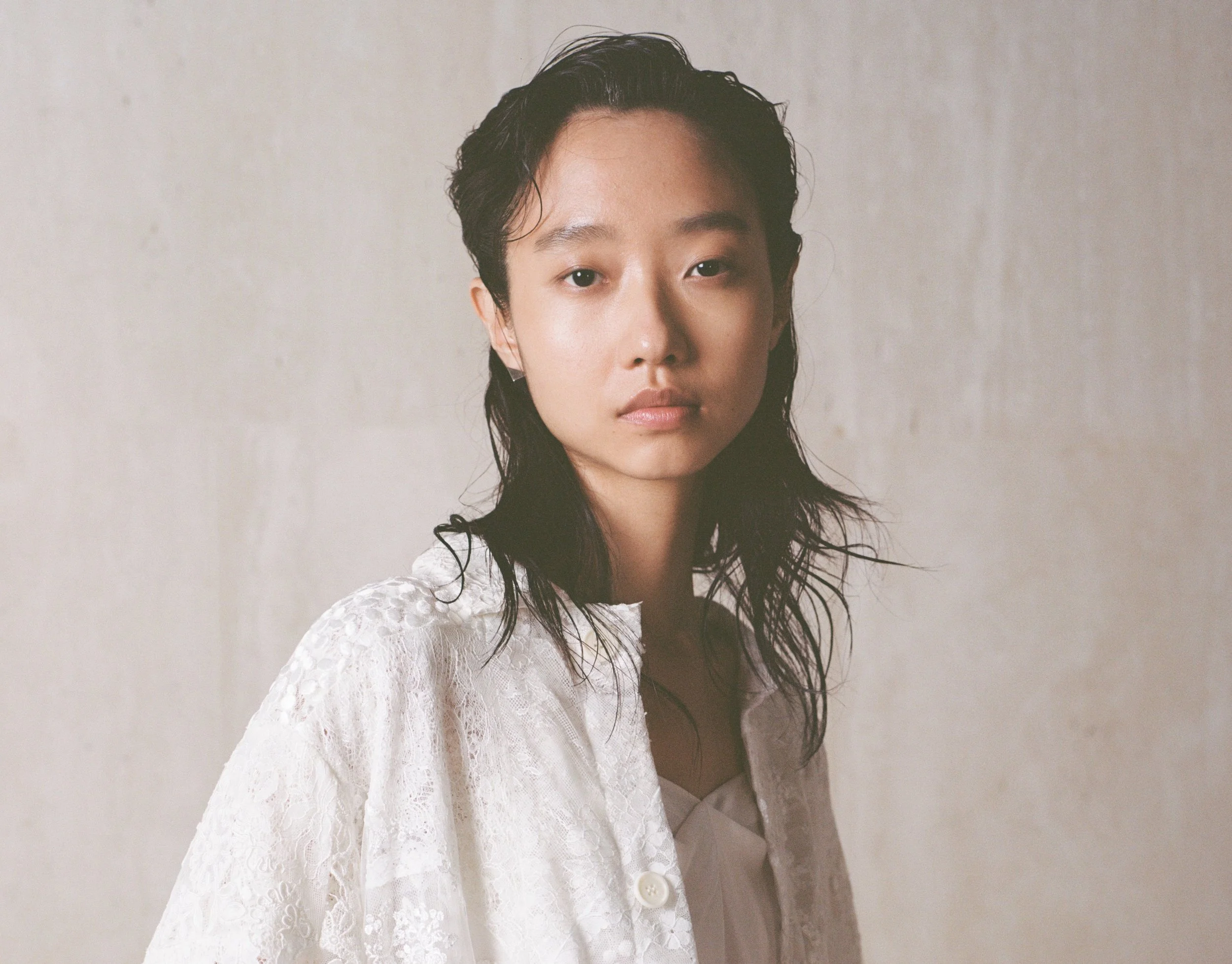Young woman in lace attire with wet hair, neutral background.