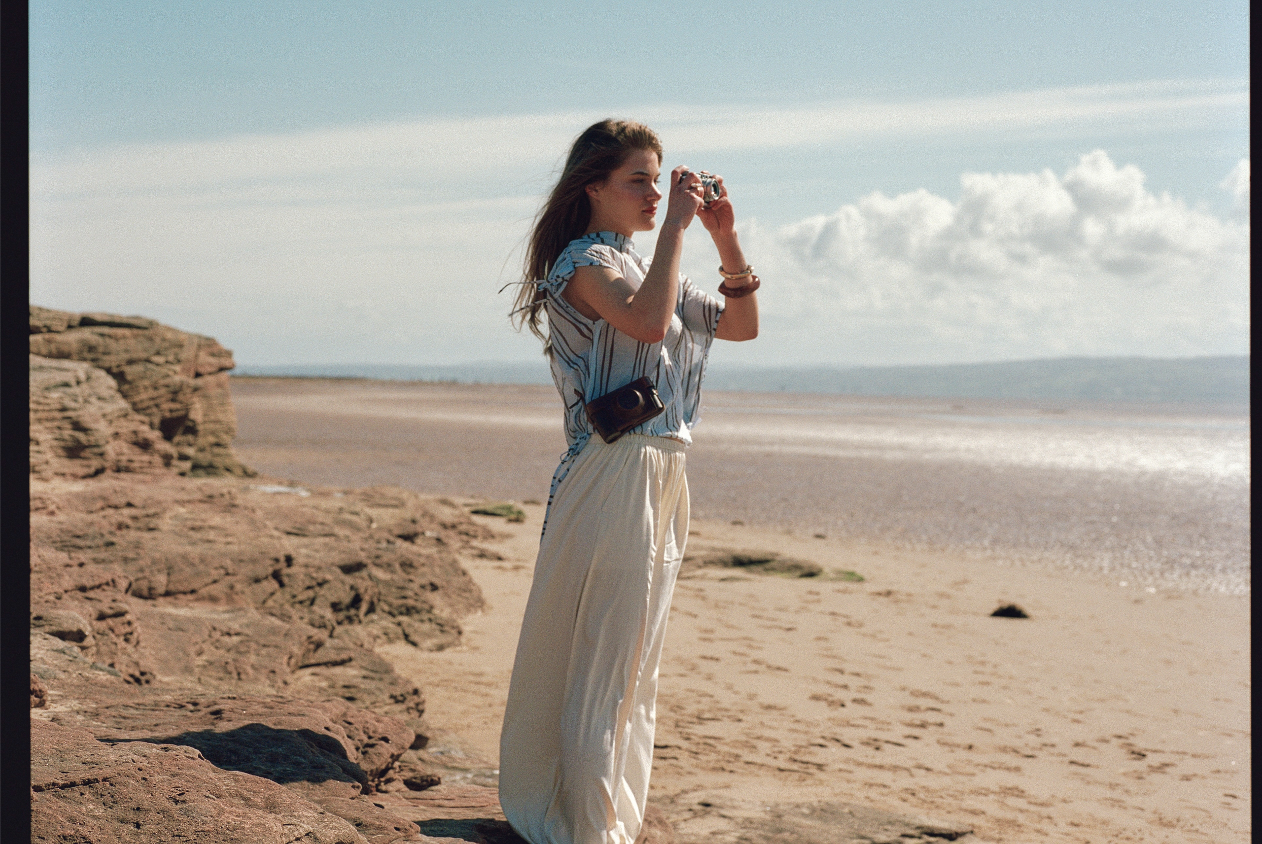 Woman taking photos on a rocky beach with a vintage camera.