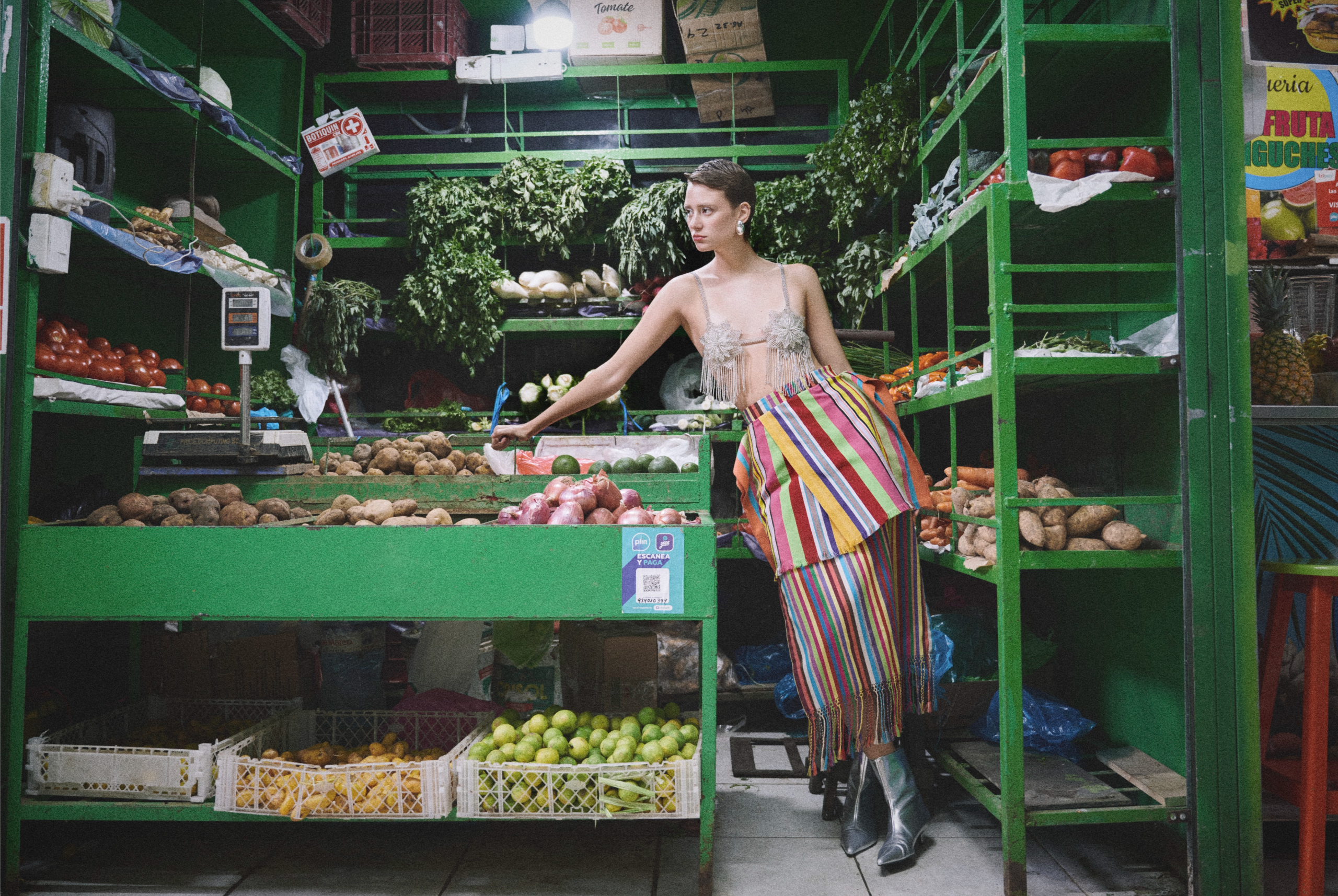Person in striped outfit standing in vibrant green market with fresh produce.