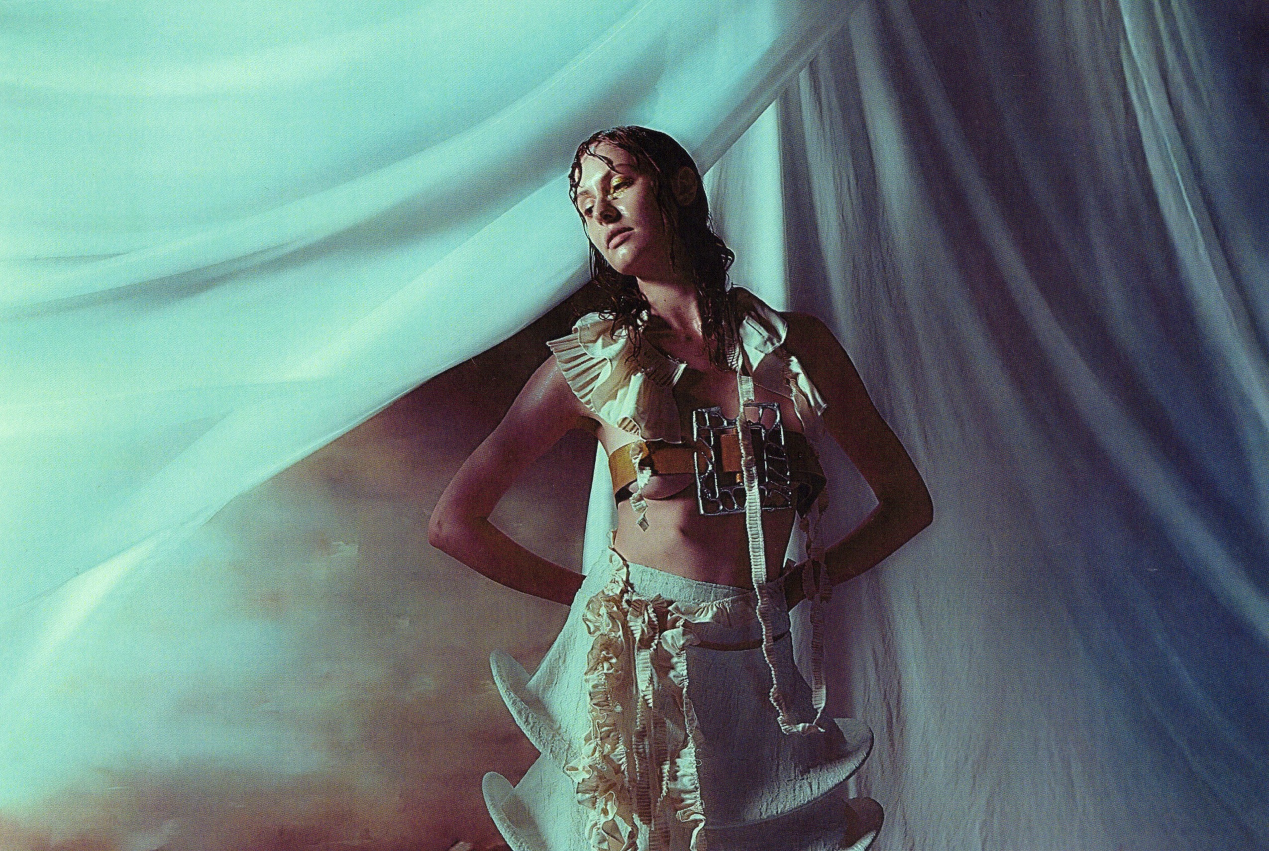 Fashion model posing in a creative, flowing outfit with draped fabric backdrop.