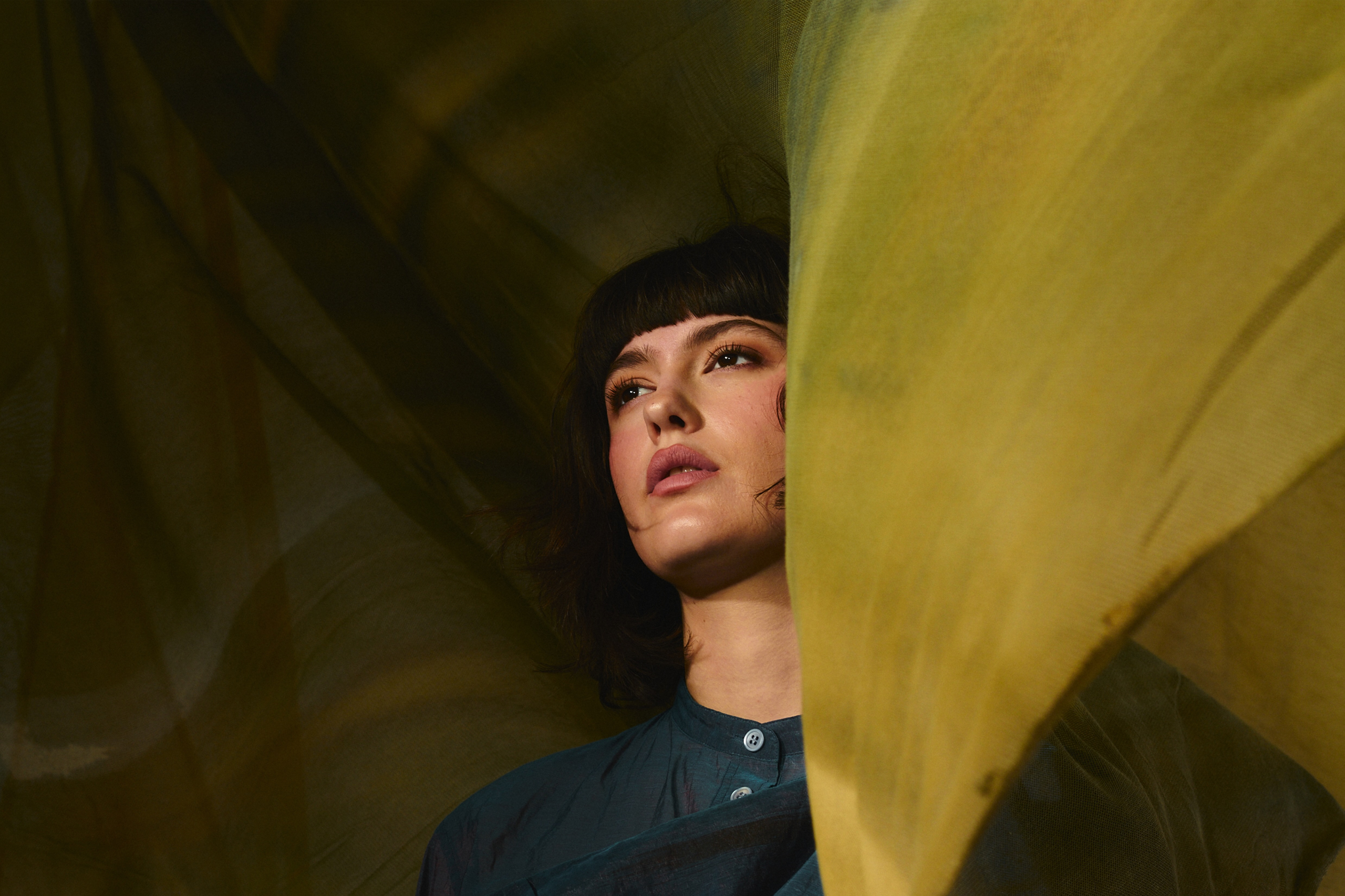 Person gazing through flowing yellow fabric in artistic portrait with soft lighting.