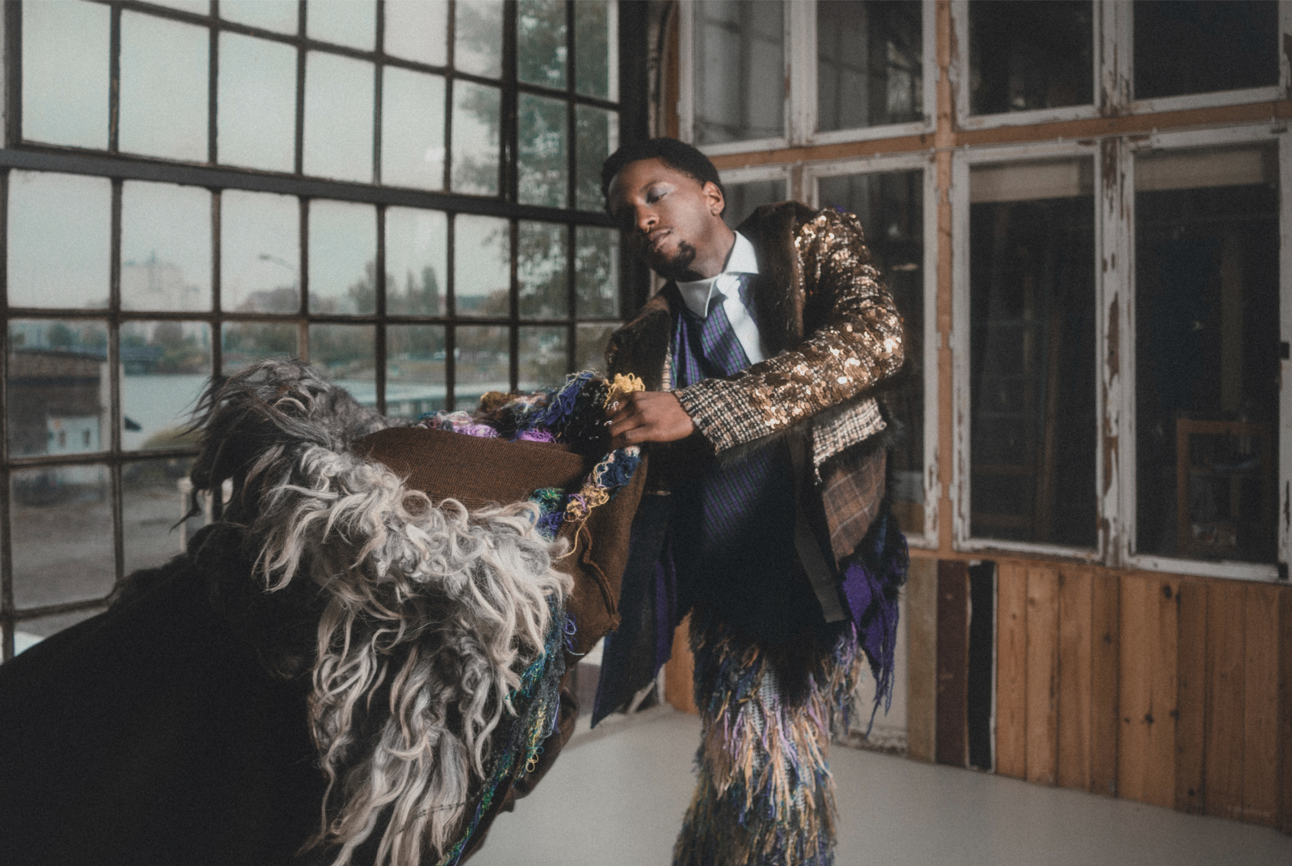 Man in eclectic fashion poses artistically by large window.