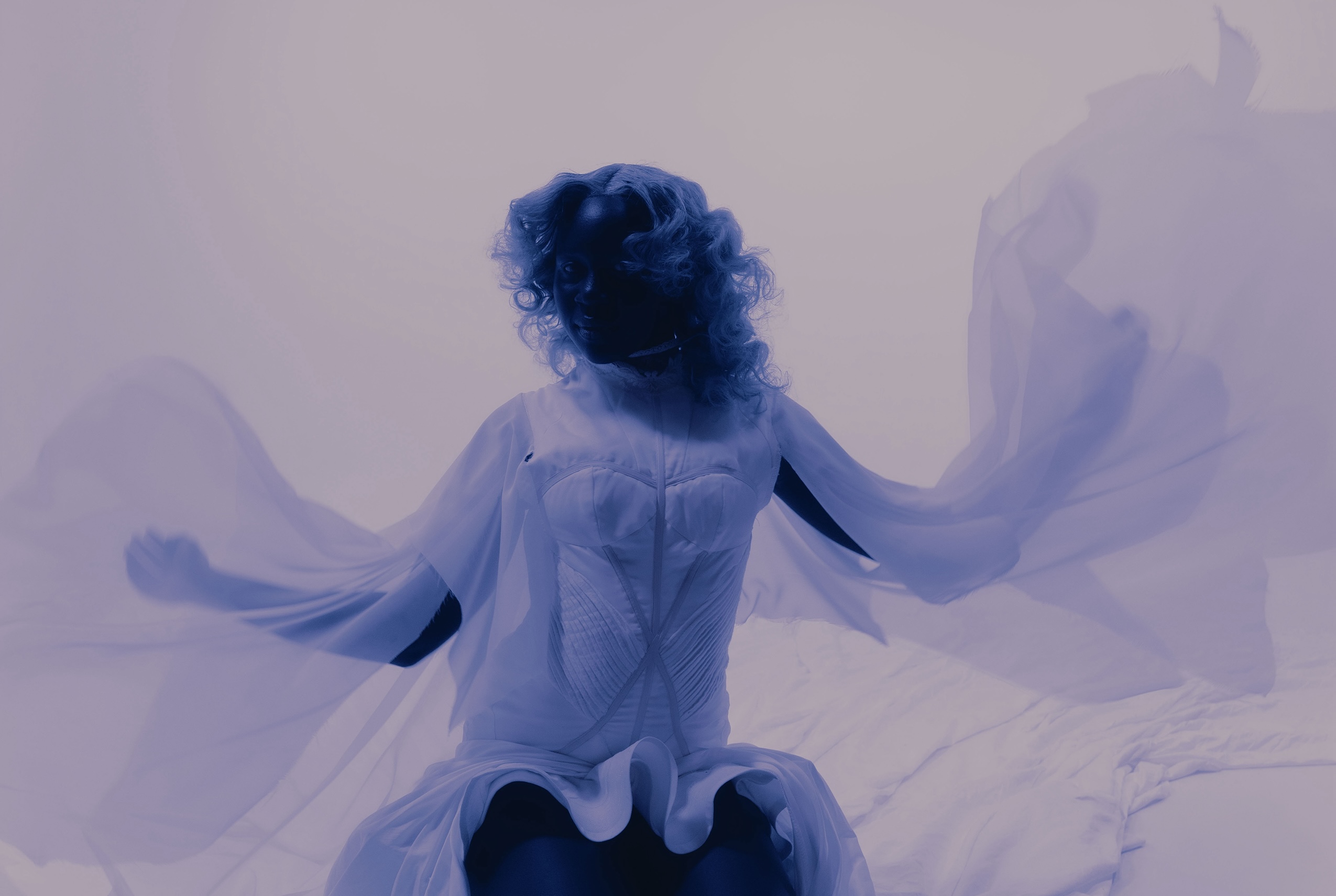 Mystical figure in a flowing dress with sheer fabric, set against a soft purple backdrop.